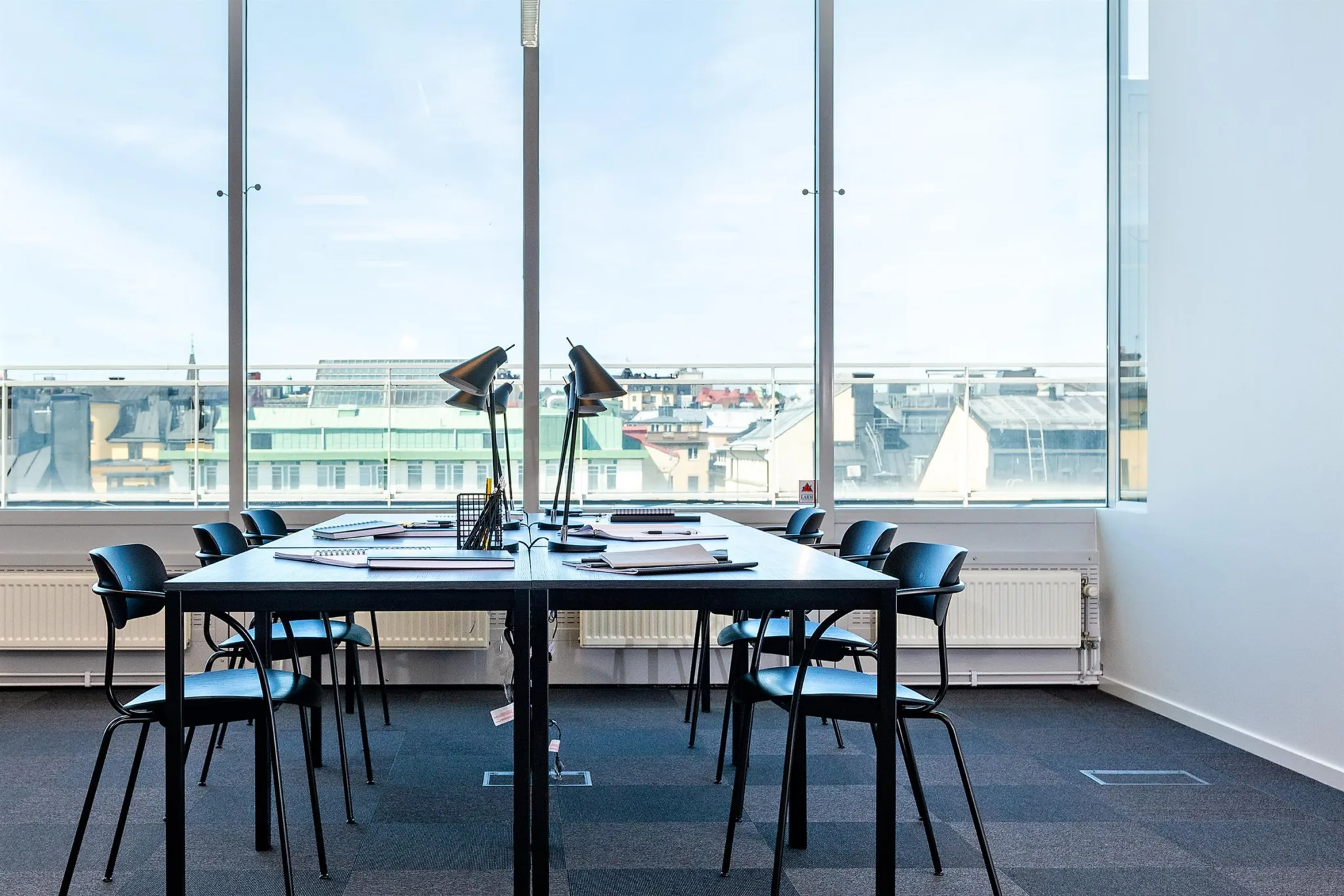 Konferensrum med ett stort bord, flera stolar och stora fönster med utsikt över stadens tak.