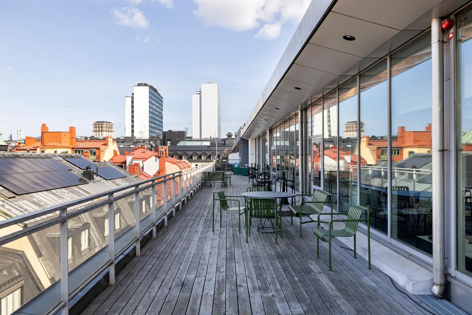 En stor takterrass med trätrall, bord och stolar, med utsikt över stadens höghus och tak.
