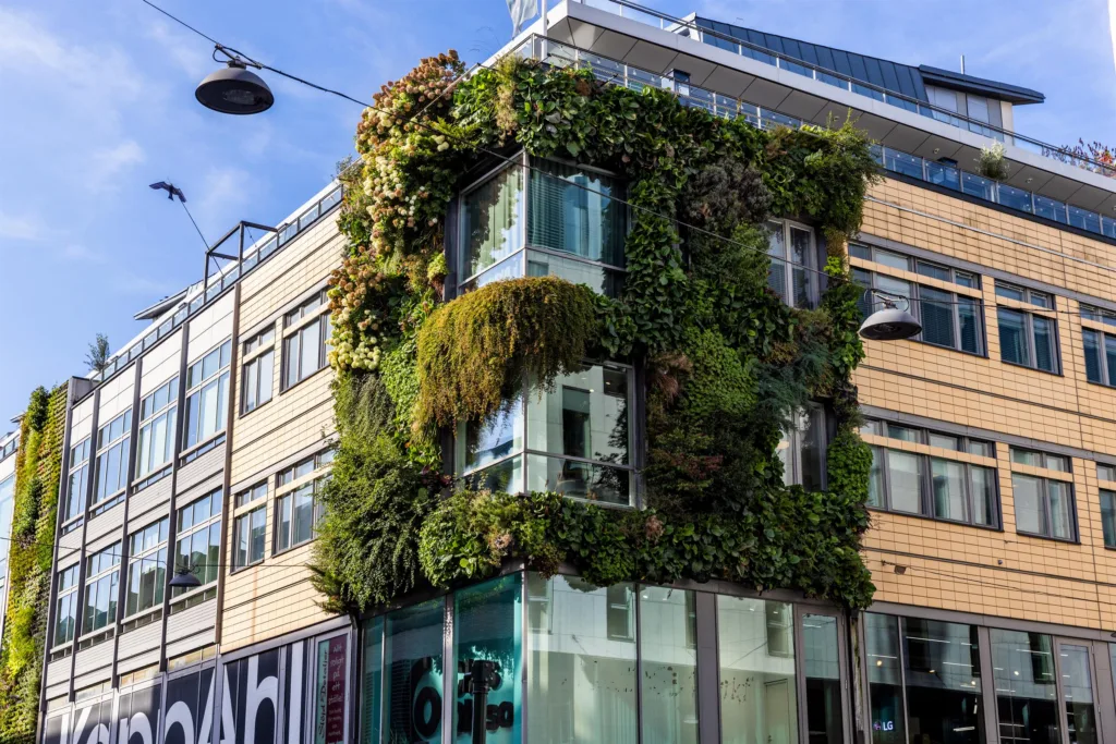 En byggnad med fasad täckt av grönska och växter, med glasfönster och modern arkitektur.