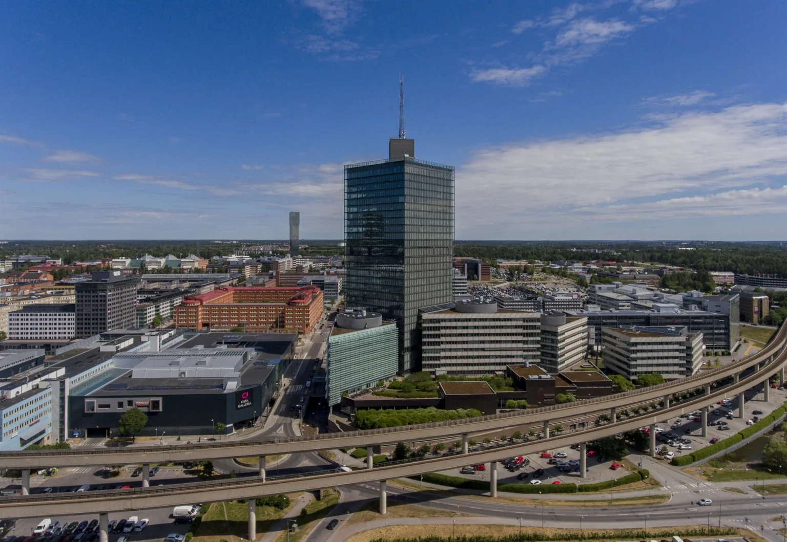 En stadsvy med höga byggnader, inklusive en skyskrapa, omgiven av vägar och grönområden.