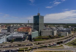 En stadsvy med höga byggnader, inklusive en skyskrapa, omgiven av vägar och grönområden.