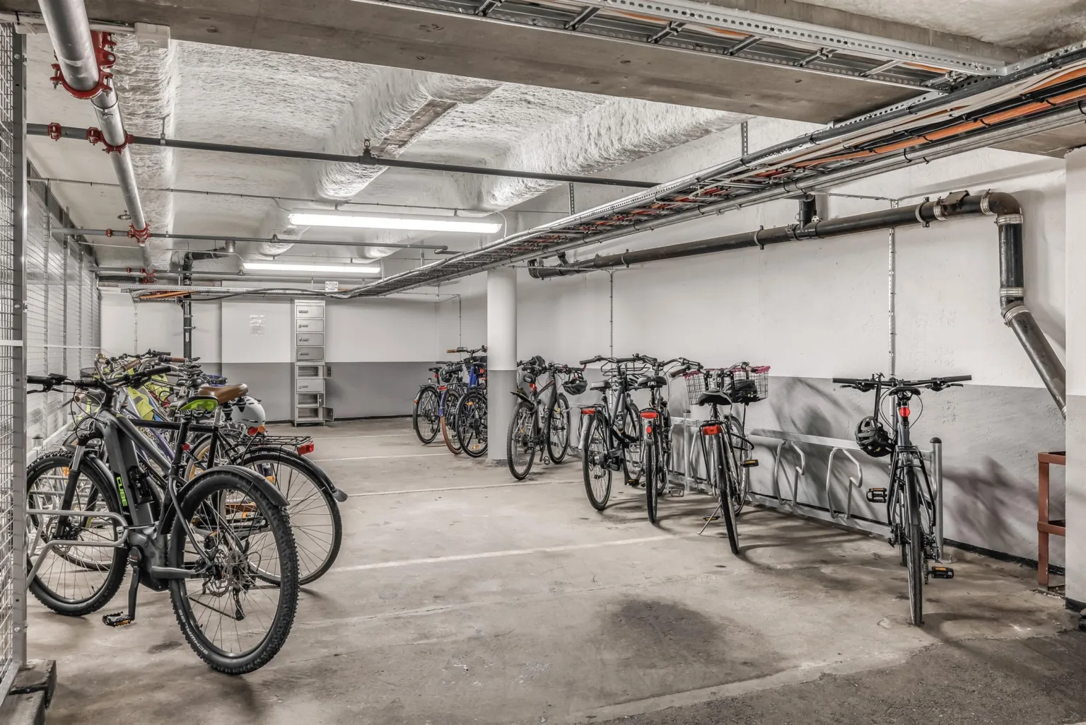 En cykelparkering inomhus med rader av parkerade cyklar och vita väggar.