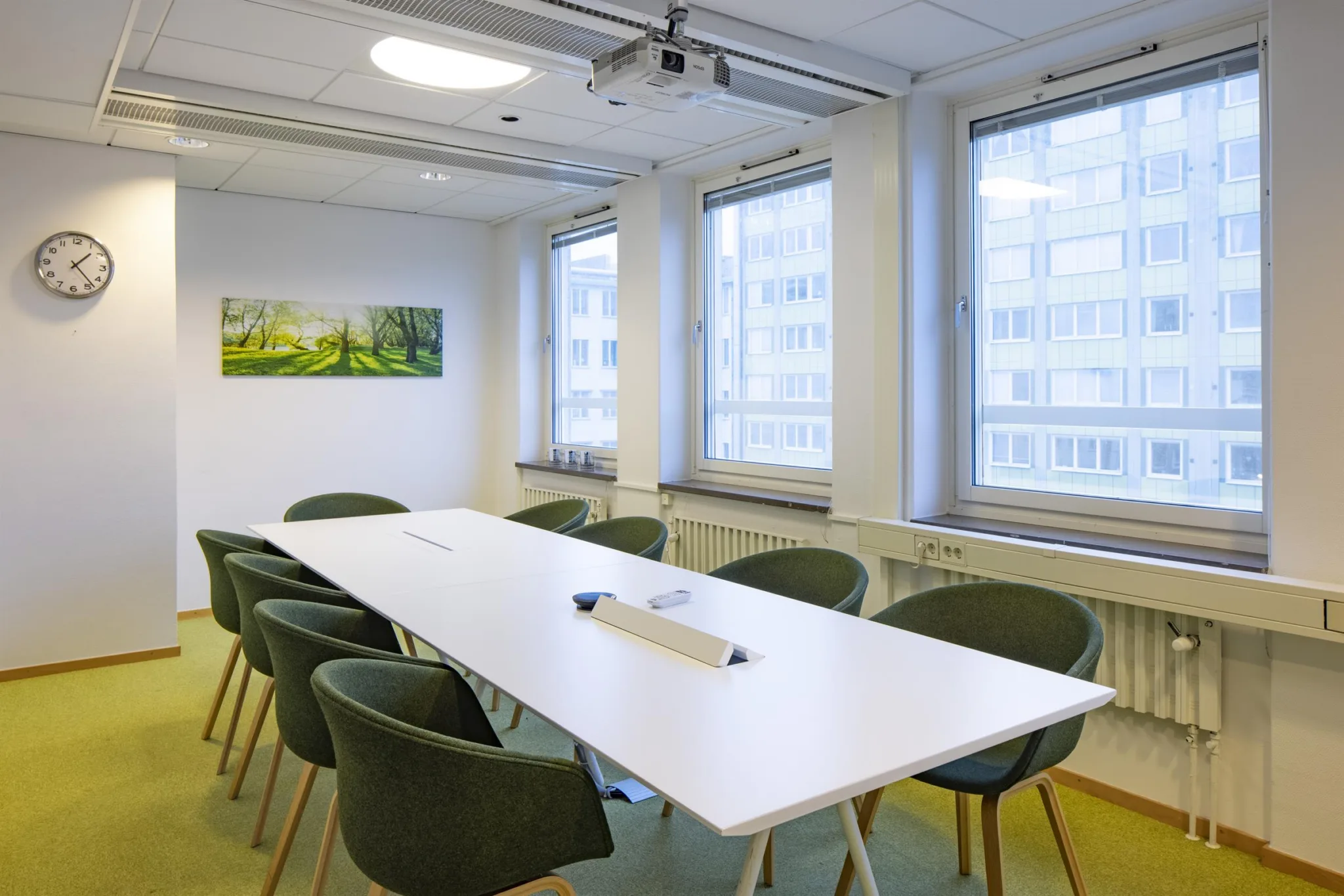 3. Ett konferensrum med ett vitt bord, gröna stolar och stora fönster.