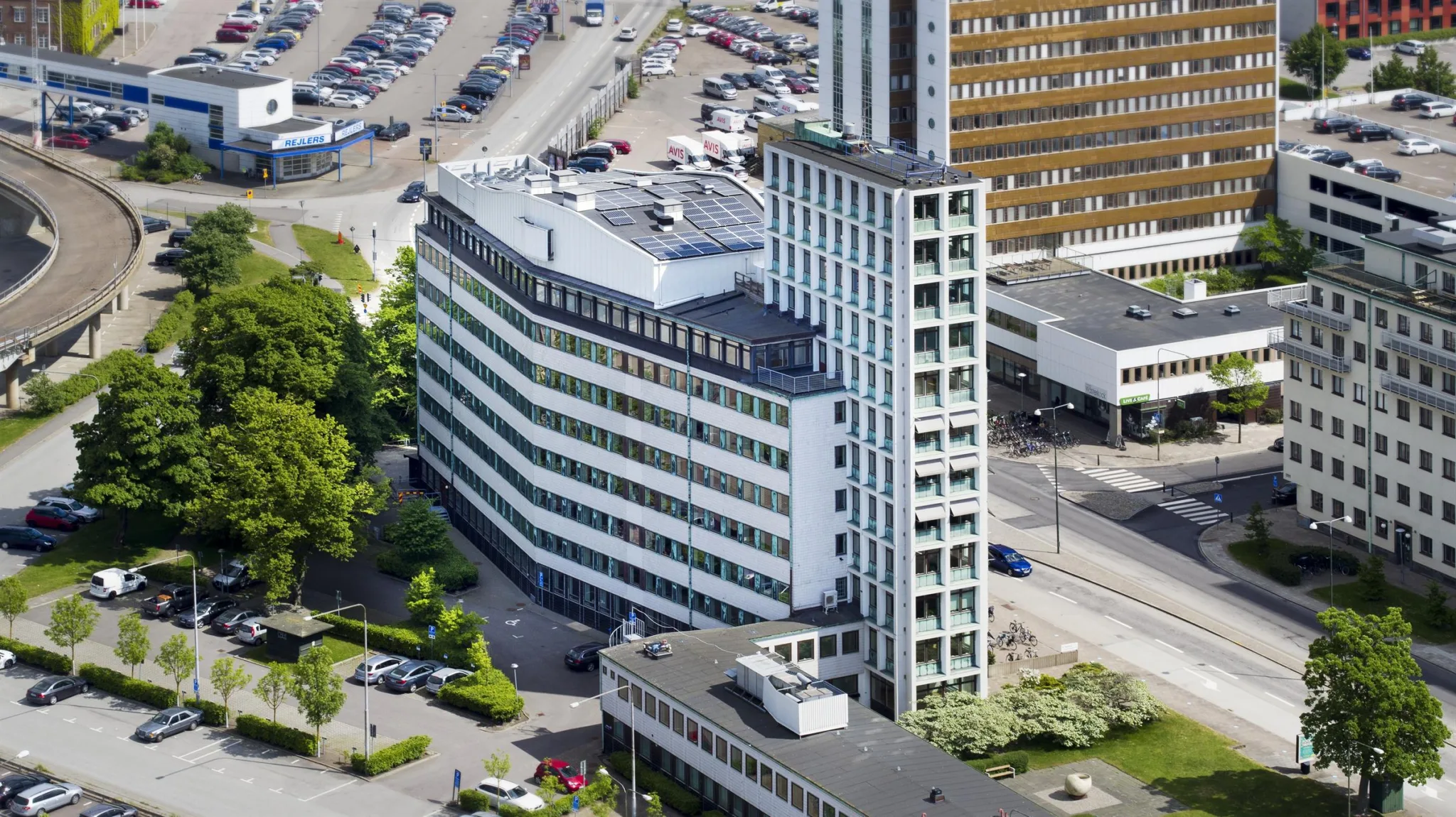 En hög byggnad med en modern design, omgiven av andra byggnader och parkeringsplatser.