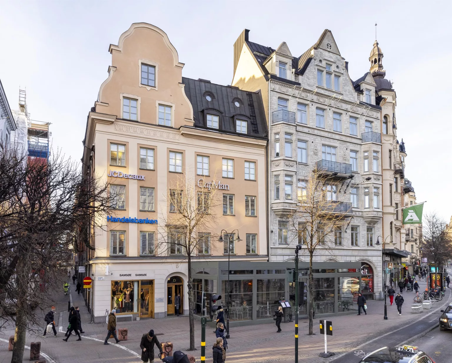 2. Flera byggnader i klassisk stil med butiker på bottenvåningen och människor som promenerar förbi på en stadsgata.