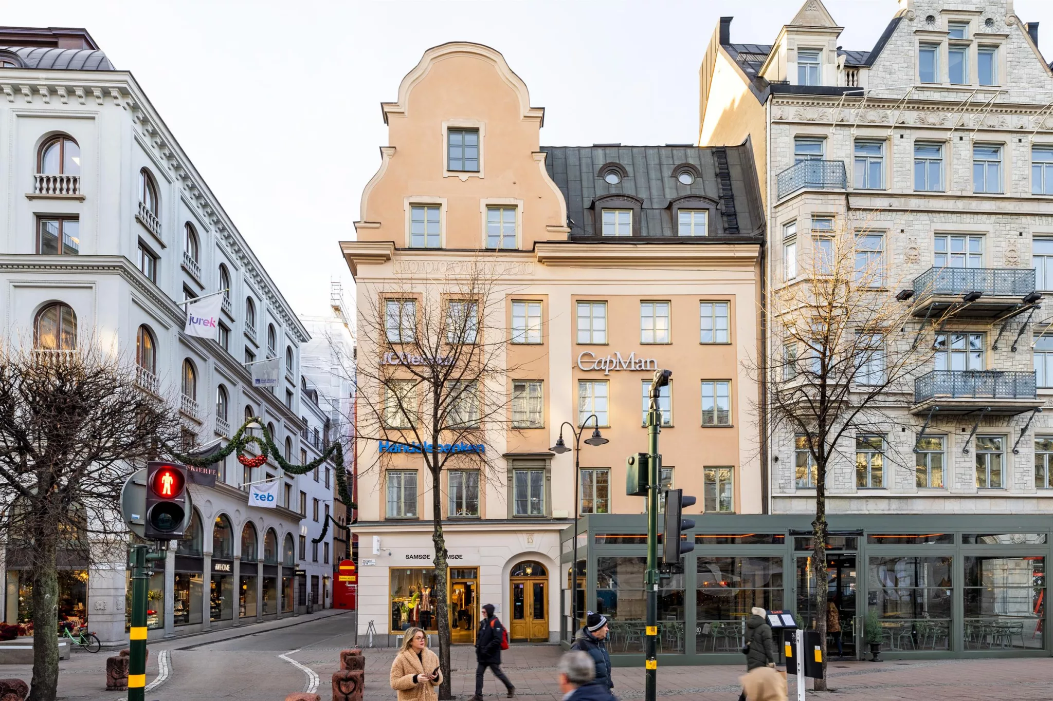 3. En beige byggnad med en gavel, butiker på bottenvåningen, och människor som går på trottoaren.