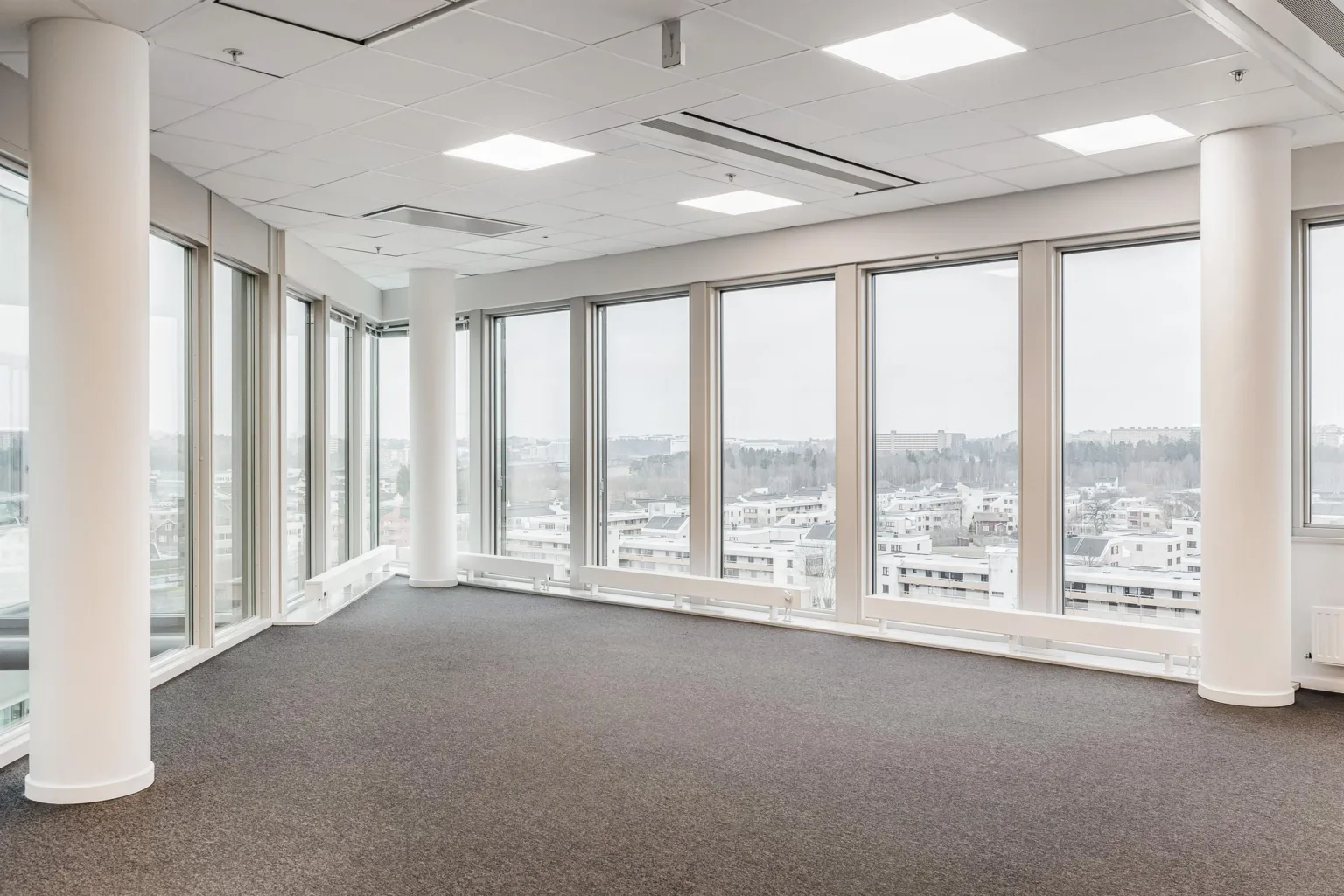 Ett tomt kontorsutrymme med mörk matta, stora fönster och en panoramautsikt över staden.