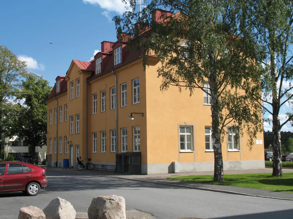 4. En gul byggnad med röda tak och fönster, omgiven av en björk och en parkerad röd bil.