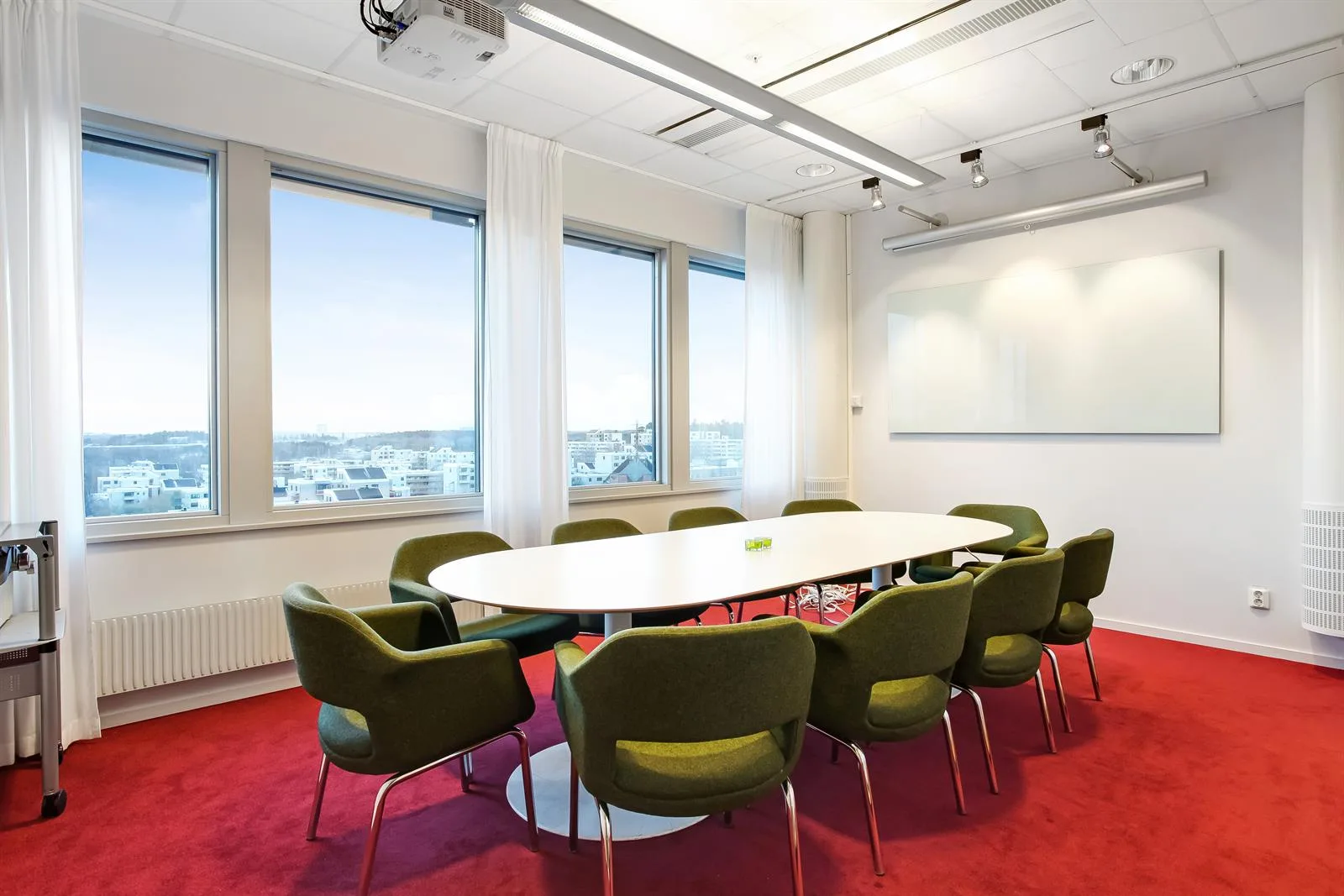 Ett konferensrum med ett ovalt bord omgivet av gröna stolar, stora fönster och röd matta.