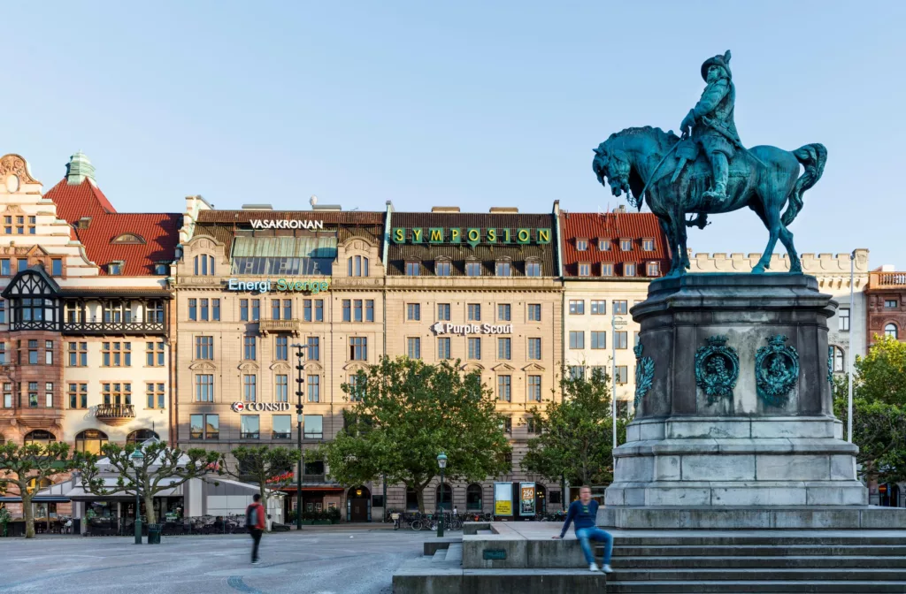 En staty av en ryttare på en häst på ett torg med äldre byggnader i bakgrunden. Skylten "Stadsmission" syns på en av byggnaderna.