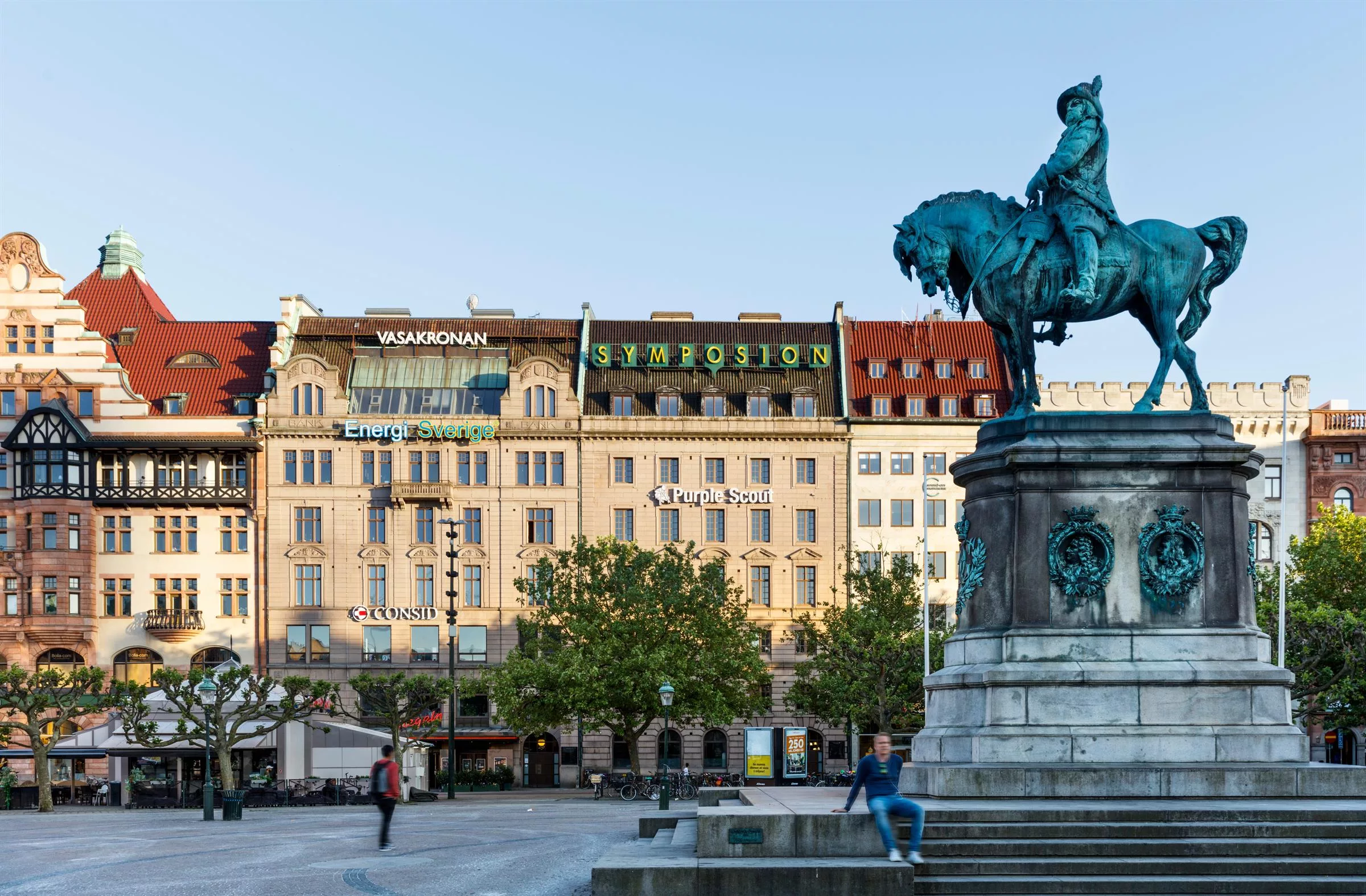 En staty av en ryttare på en häst på ett torg med äldre byggnader i bakgrunden. Skylten "Stadsmission" syns på en av byggnaderna.