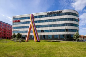 En byggnad med fasadskyltar för Vasakronan och andra företag, en stor färgglad rosett står på gräsmattan framför byggnaden.