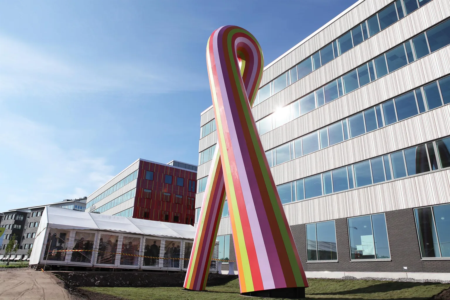 En stor utomhus skulptur i form av en färgglad rosett framför en modern byggnad med glasfasad.