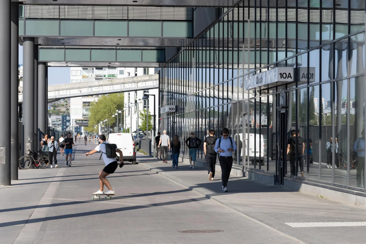 En stadsgata med glasfasader, människor som går och en person på skateboard.