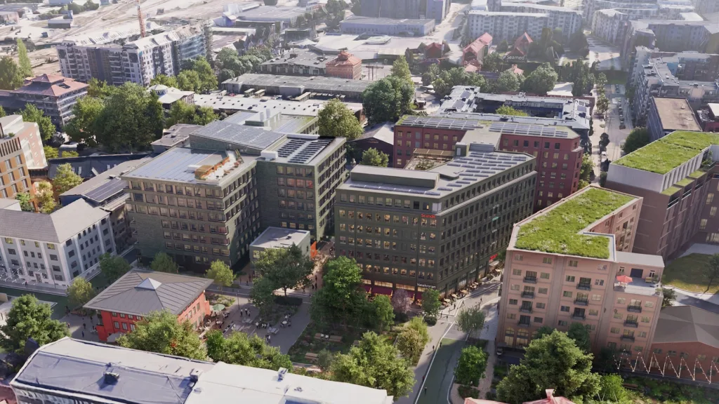 Flygvy över en stadsdel med moderna byggnader, gröna träd och grönområden.