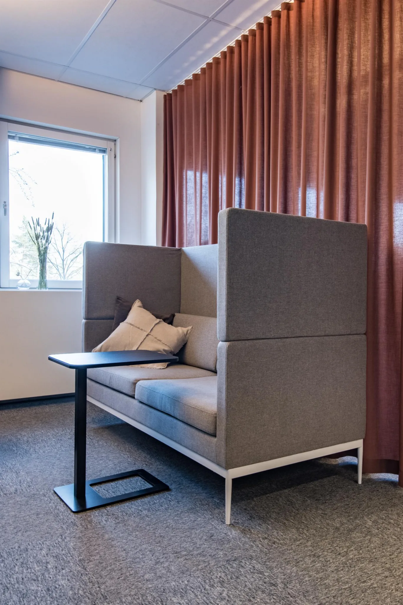 En grå sittplats med höga ryggstöd, kuddar och ett litet bord framför.
