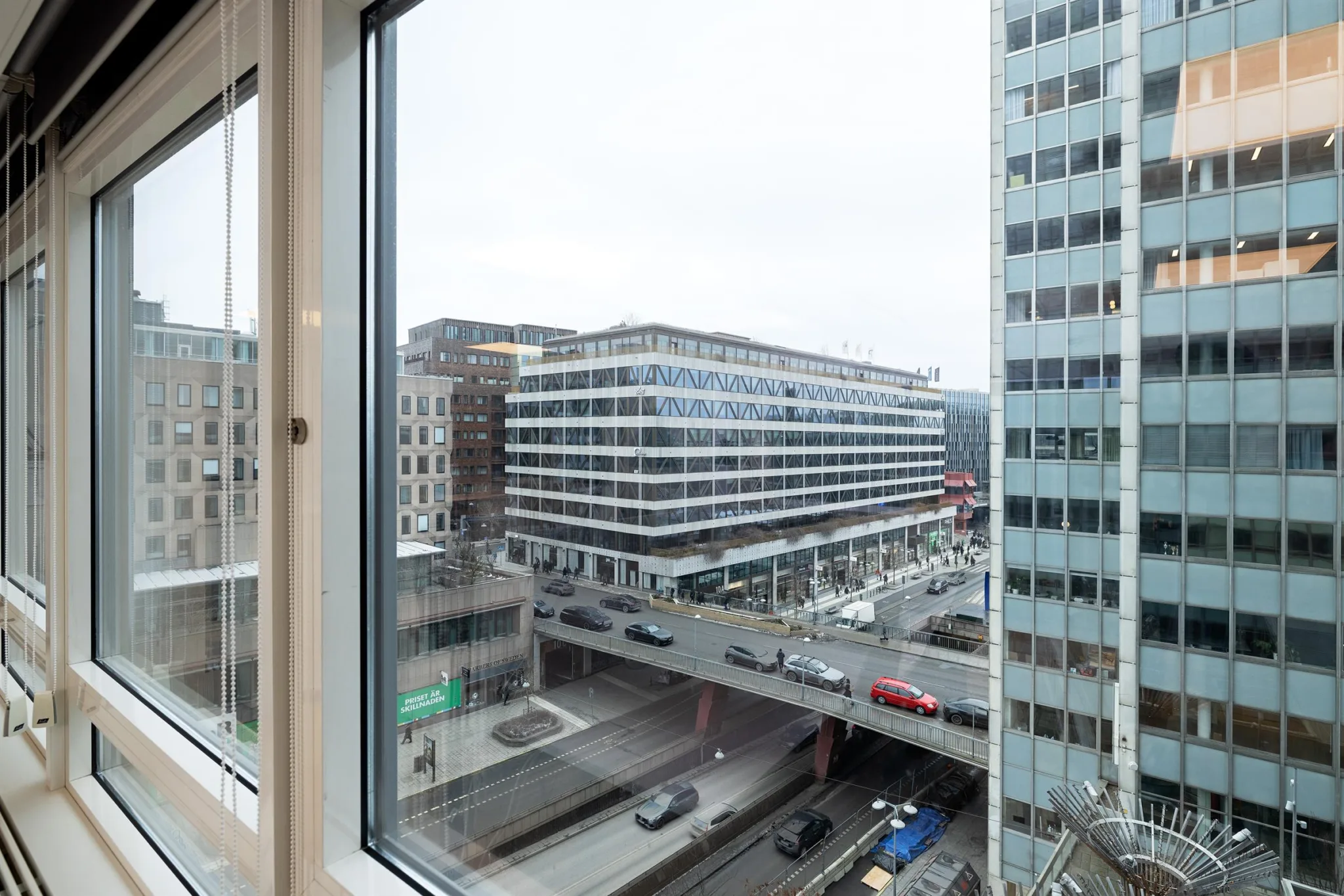Utsikt från ett fönster mot en stadsgata med bilar och moderna byggnader.