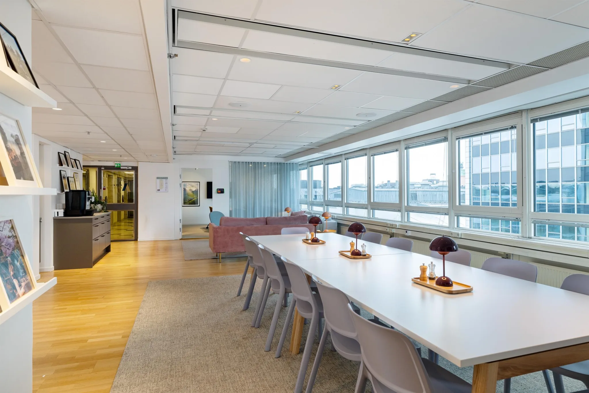Ljus och rymlig mötesplats med ett långt bord, stolar och dekorationer, samt stora fönster med utsikt över staden.