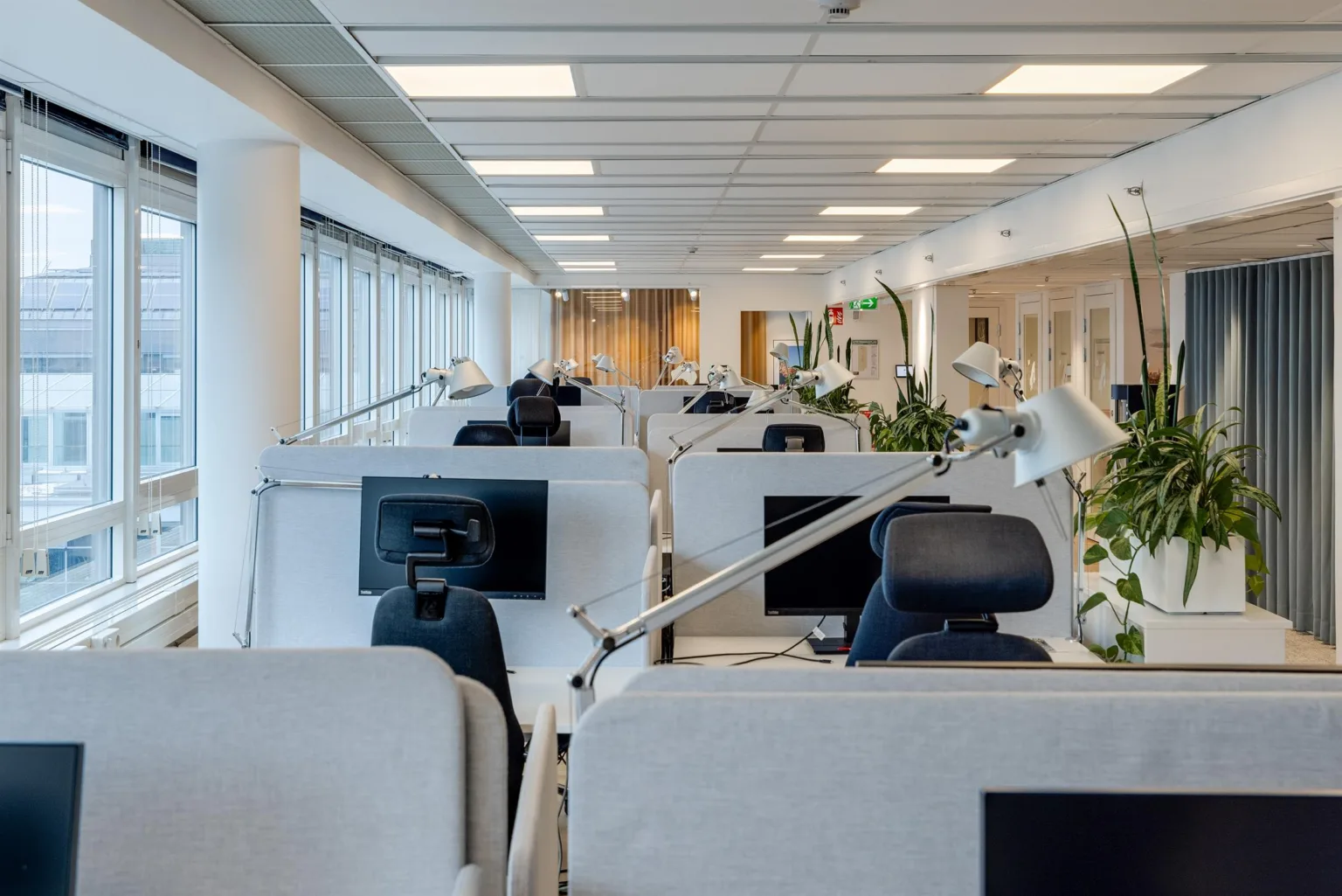 Flera arbetsstationer med skrivbord, kontorsstolar och datorskärmar, ordnade i rader i en ljus kontorslokal.