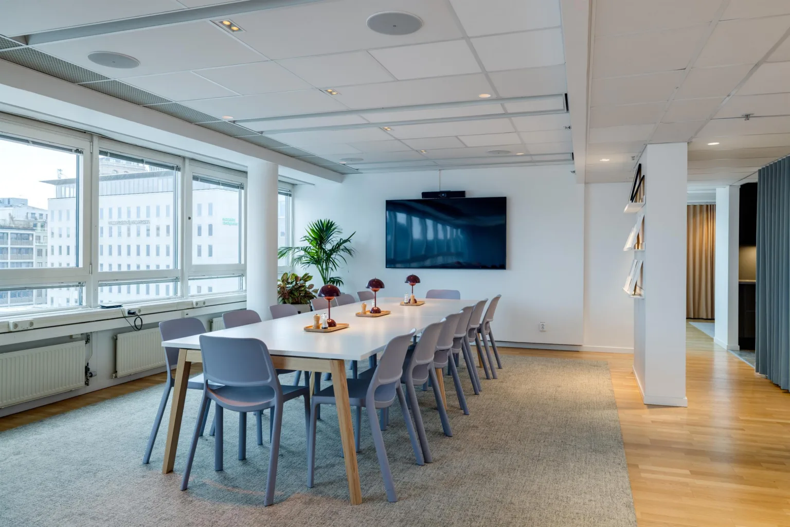 Ett modernt mötesrum med lång konferensbord, stolar och väggmonterad skärm.