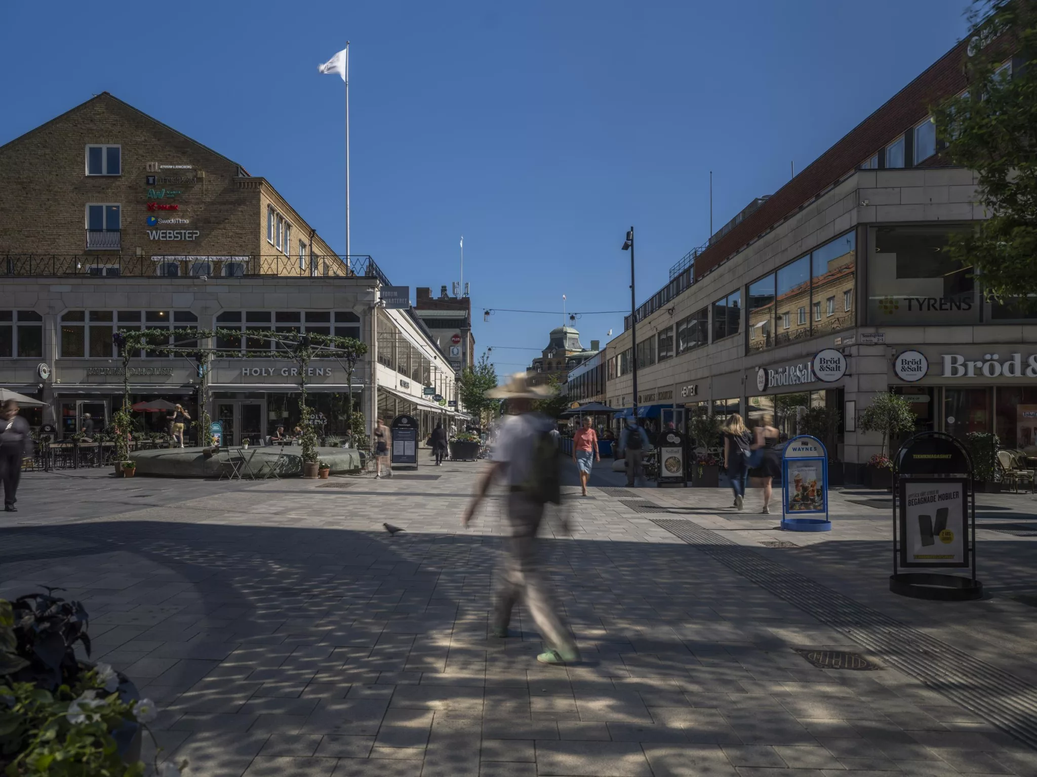 5. En gågata med byggnader på båda sidor och en person som går i förgrunden under en blå himmel.