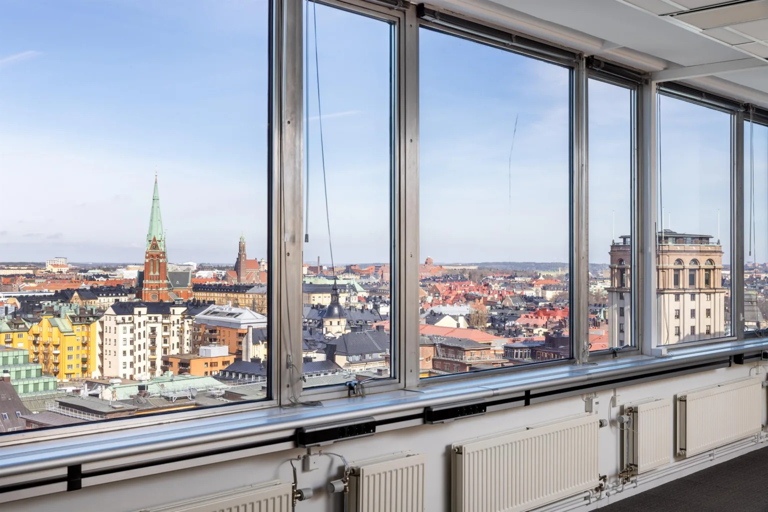 2. Utsikt över en stad med kyrktorn och byggnader, sett genom stora glasfönster från ett högt beläget rum.