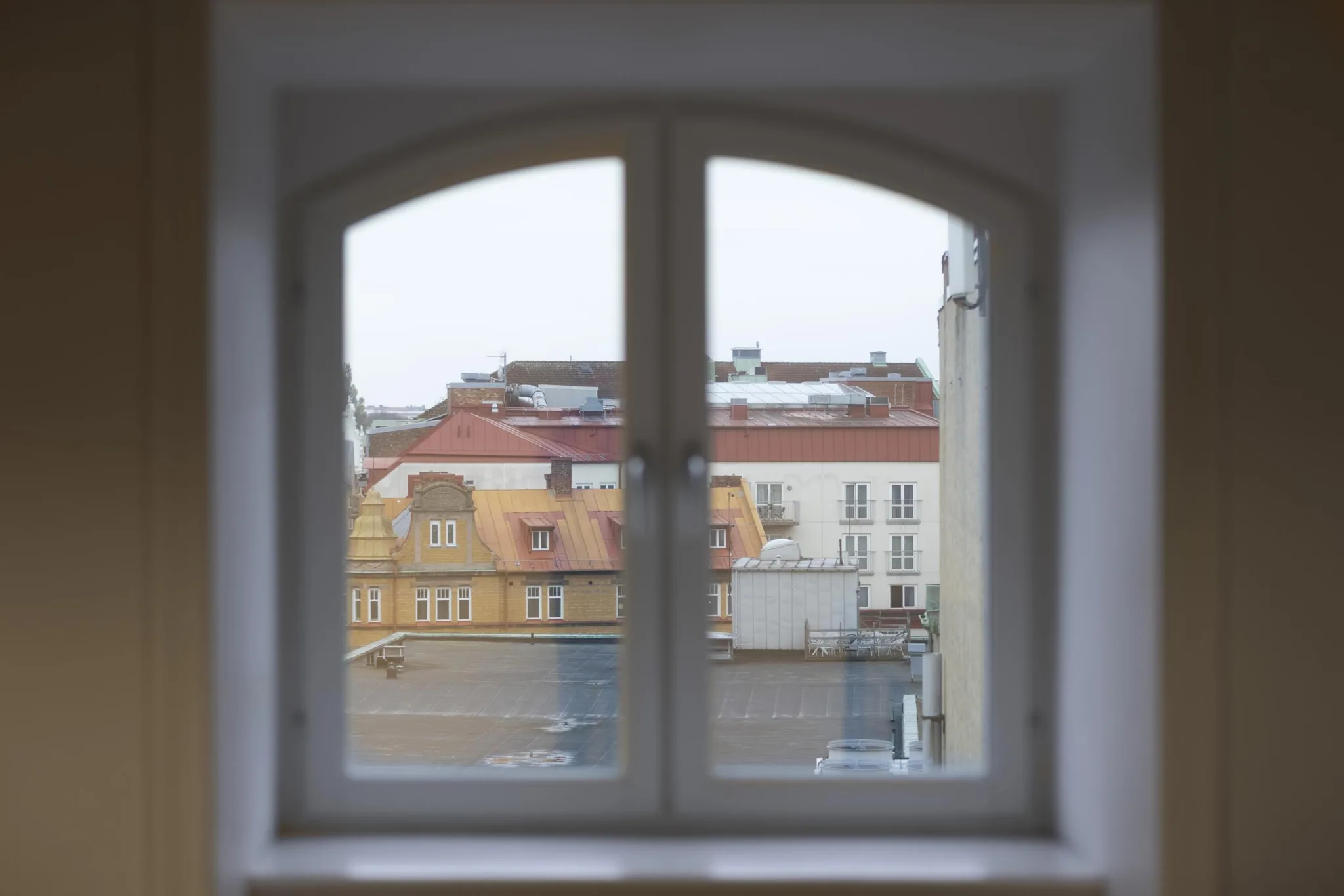 Ett välvt fönster med utsikt över tak och byggnader i en stad.