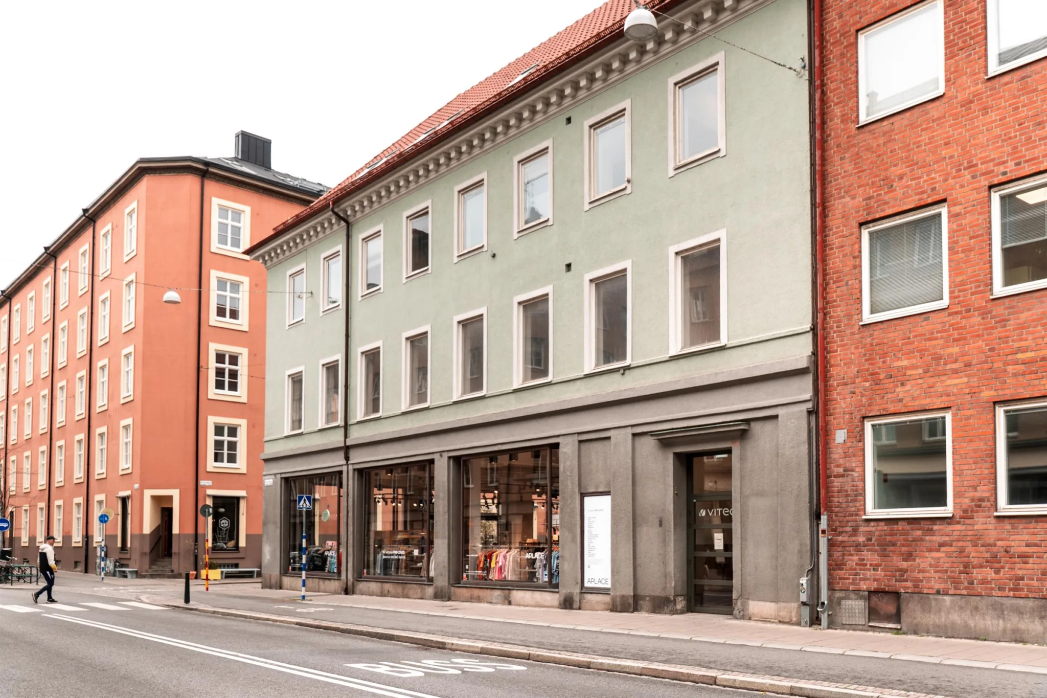 En byggnad med grön fasad och stora skyltfönster längs en stadsgata, omgiven av röda hus.
