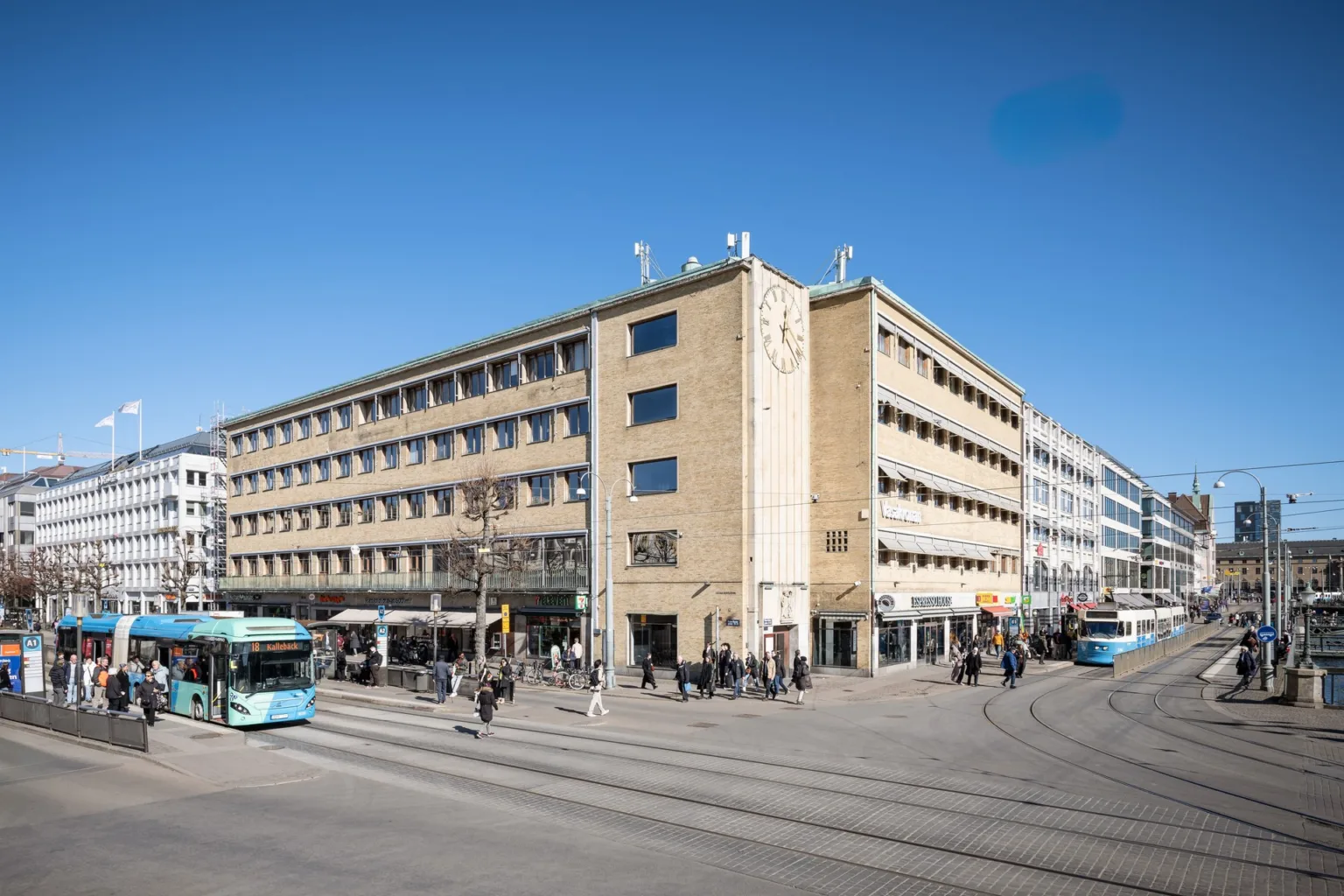 Gatuperspektiv av en fyravåningsbyggnad med butiker och människor i rörelse.