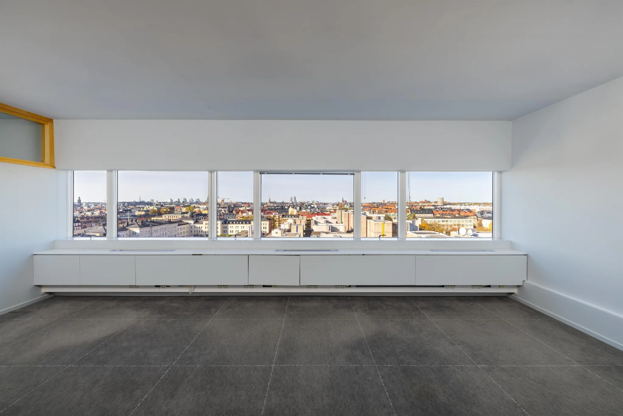 Tomt rum med mörk grå golv och stora panoramafönster som visar ett stadslandskap.