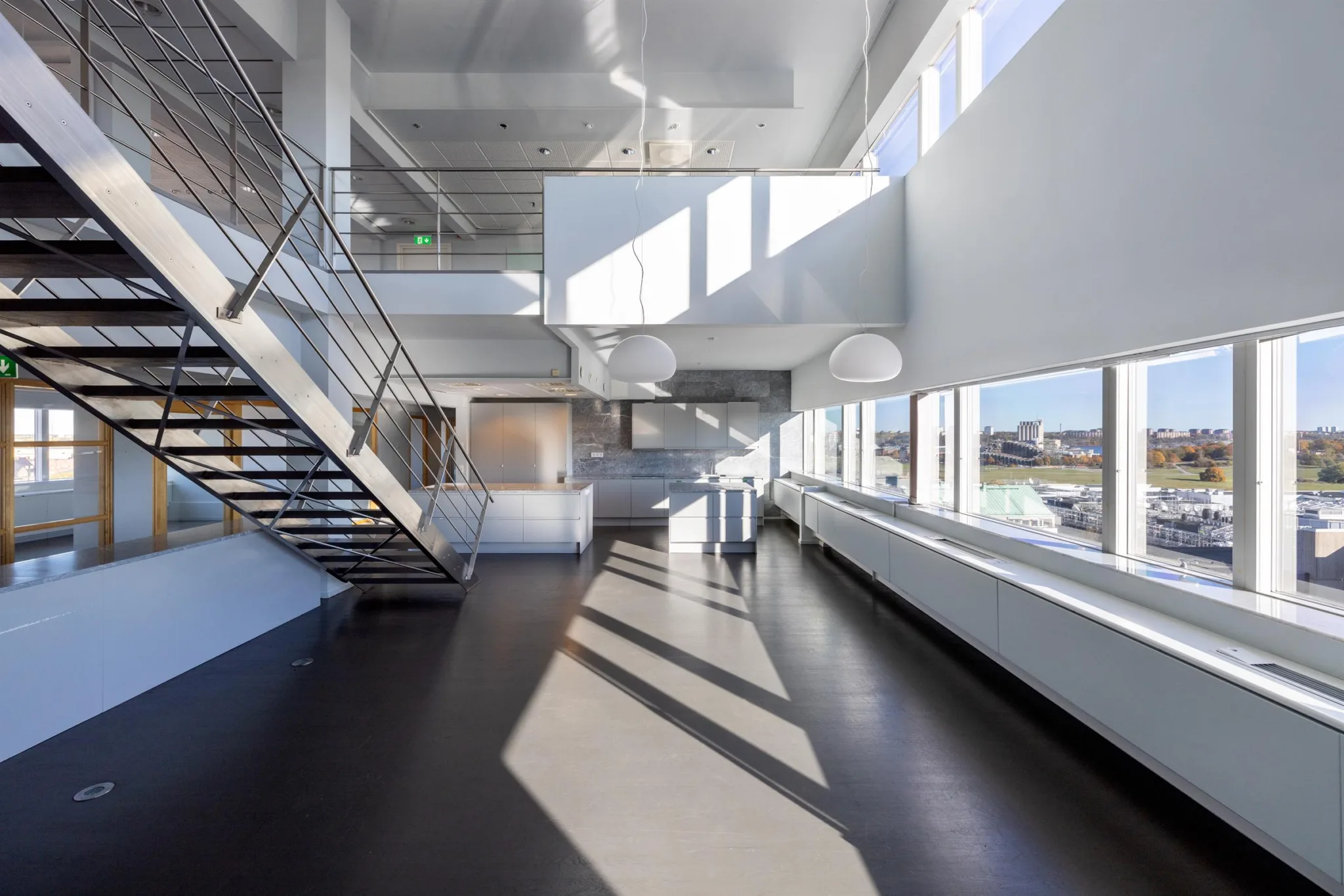 Interiör av en modern byggnad med trappa, stora fönster och solbelysta golv.
