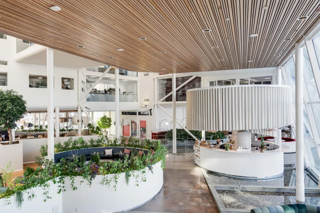 3. Ett ljust atrium med växter, högt tak i trä och en reception med rund form.