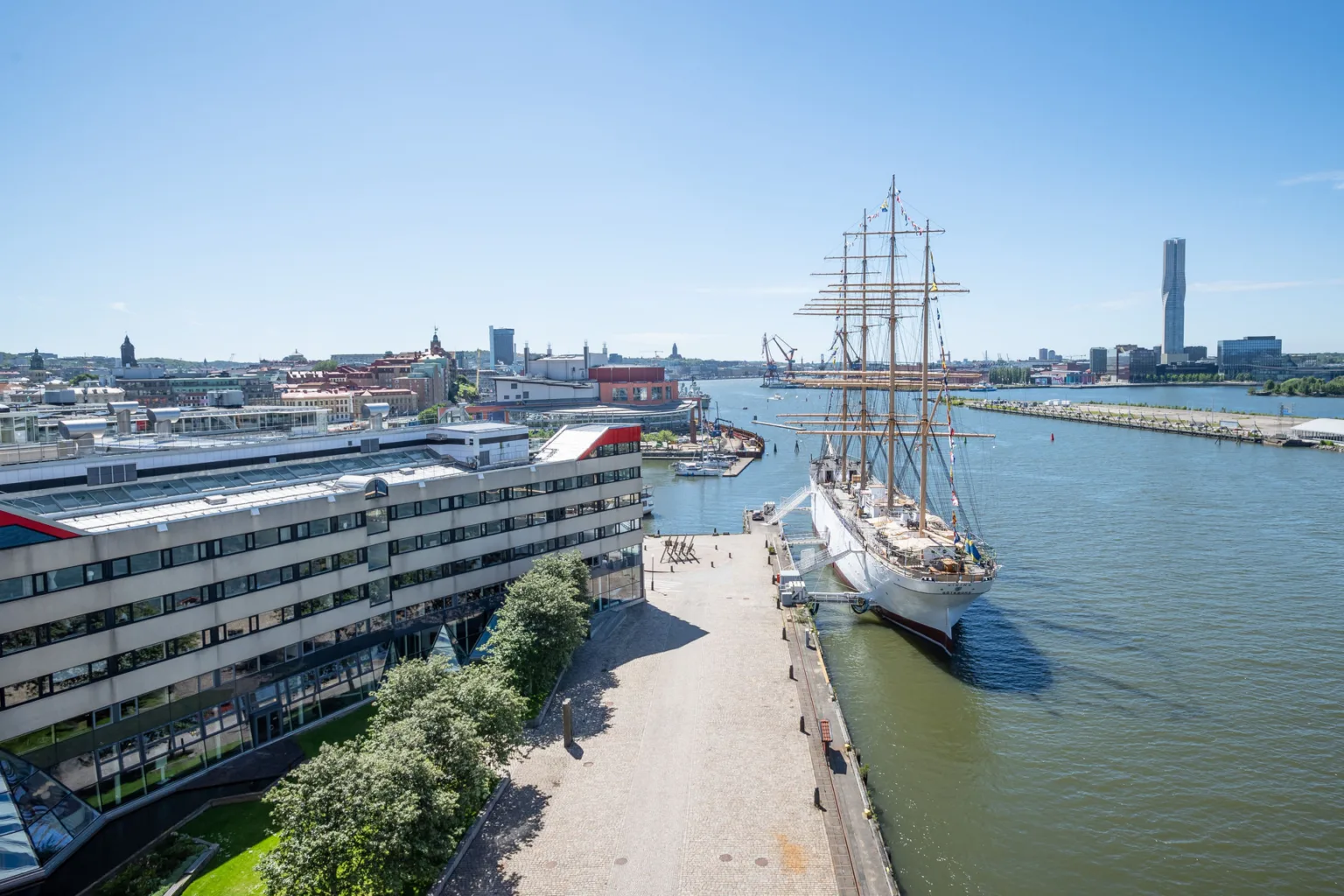 En vy över en hamn med ett stort segelfartyg och byggnader vid vattnet.