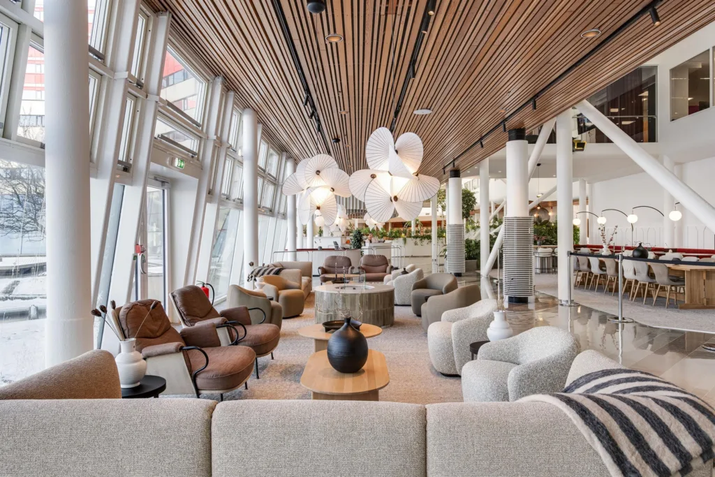 5. Ett stilrent loungeområde med träpaneler i taket, stora fönster och olika sittmöbler.