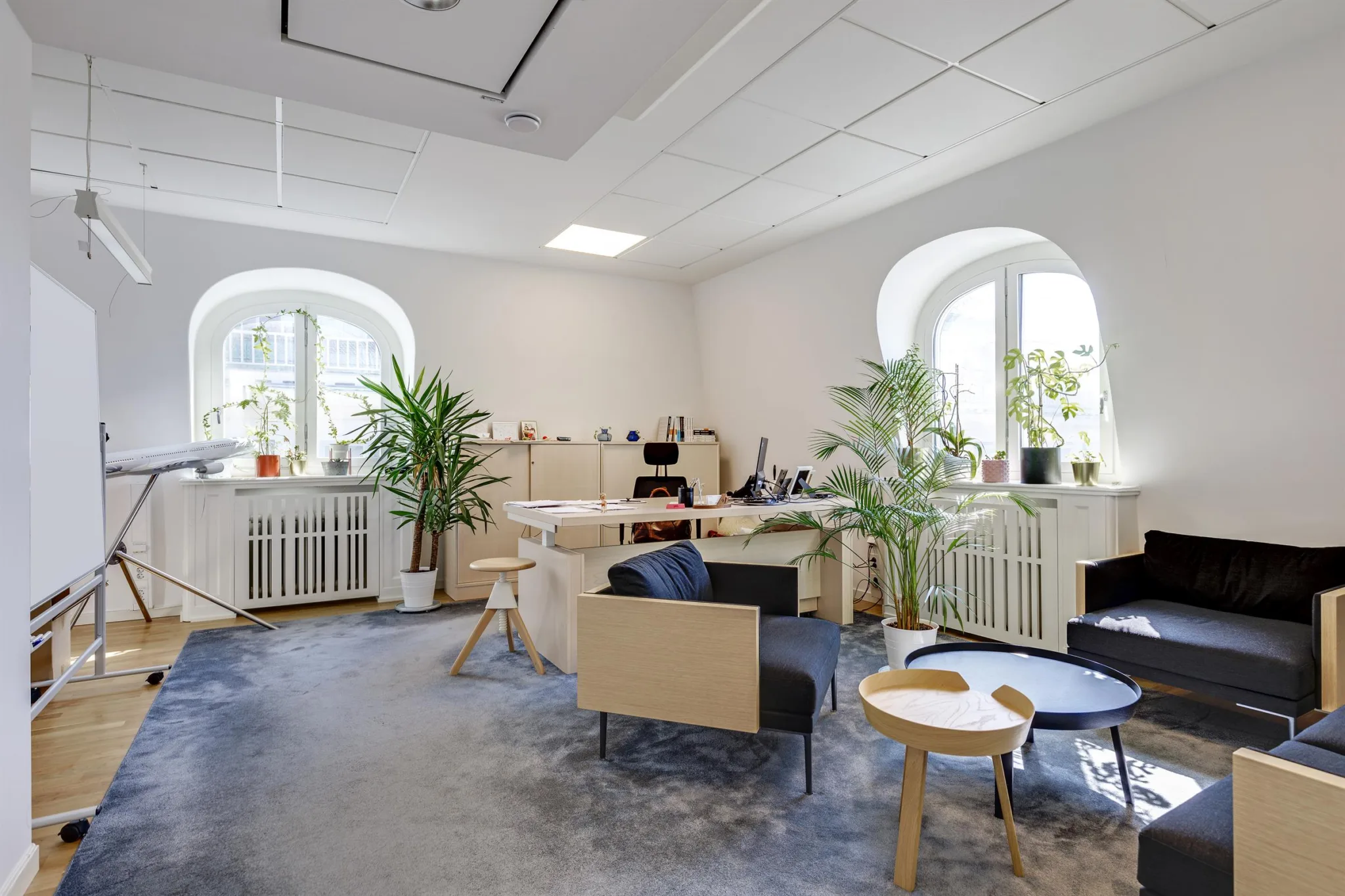Ett modernt kontorsrum med beige möbler, gröna växter och stora fönster som släpper in ljus.