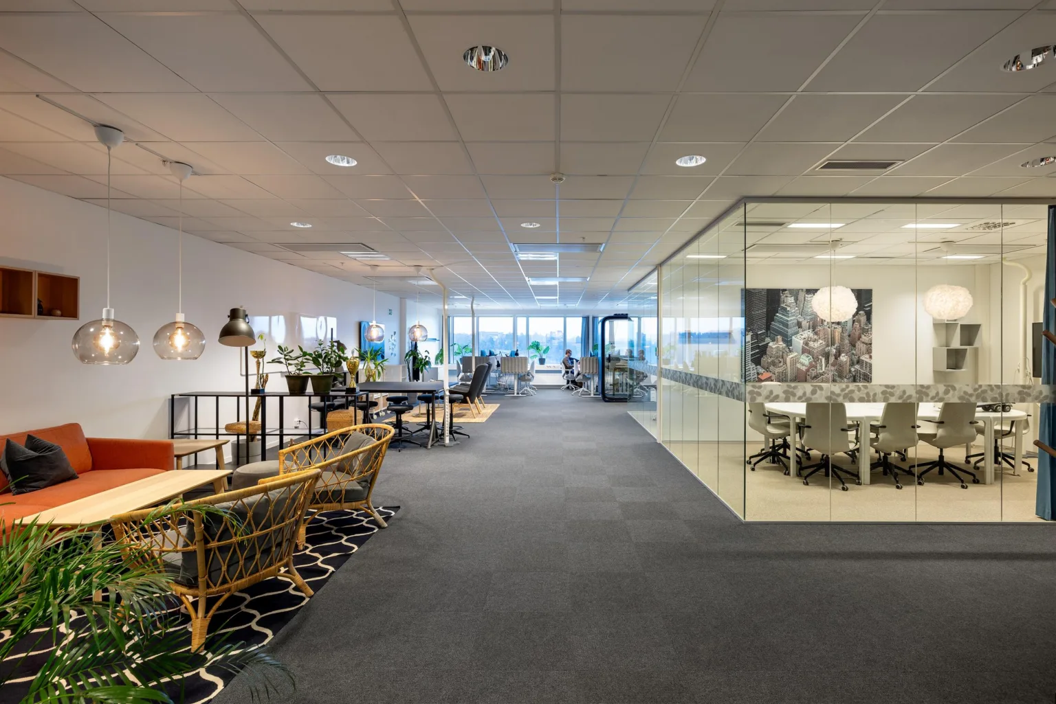 Ett modernt kontorslandskap med sittgrupper, glasväggar och ljusa möbler.