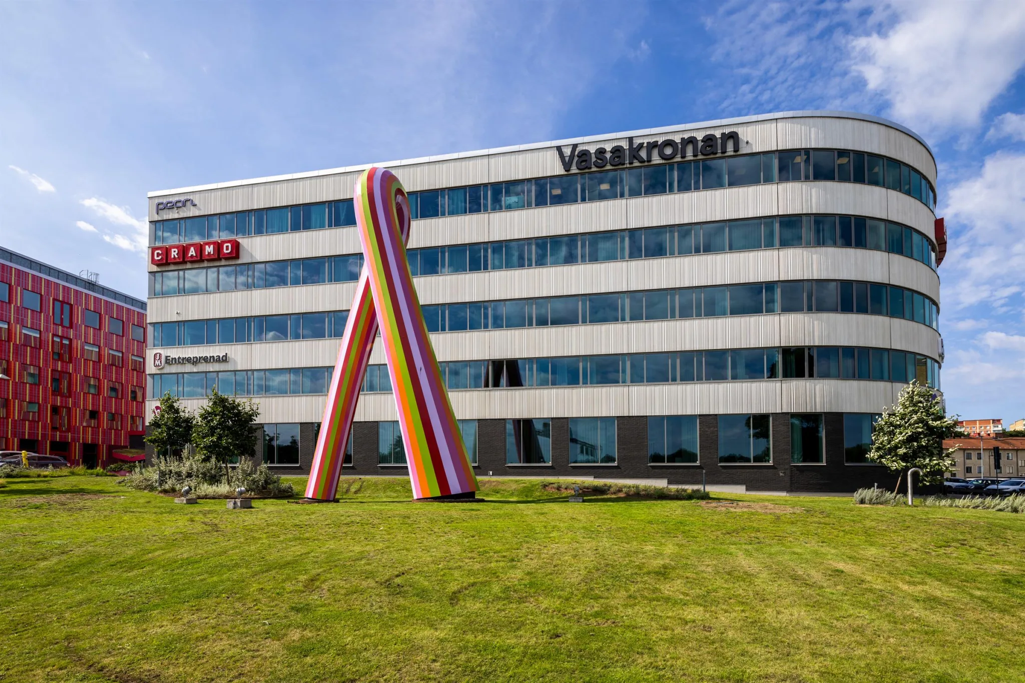 3. En stor kontorsbyggnad med fasadtexten "Vasakronan" och en färgglad skulptur framför på en grön gräsmatta.
