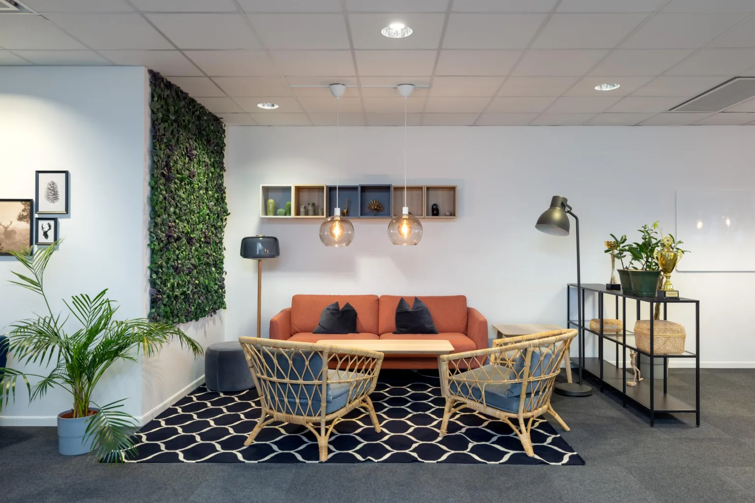 En lounge med orange soffa, rottingfåtöljer, hängande lampor och växtvägg.