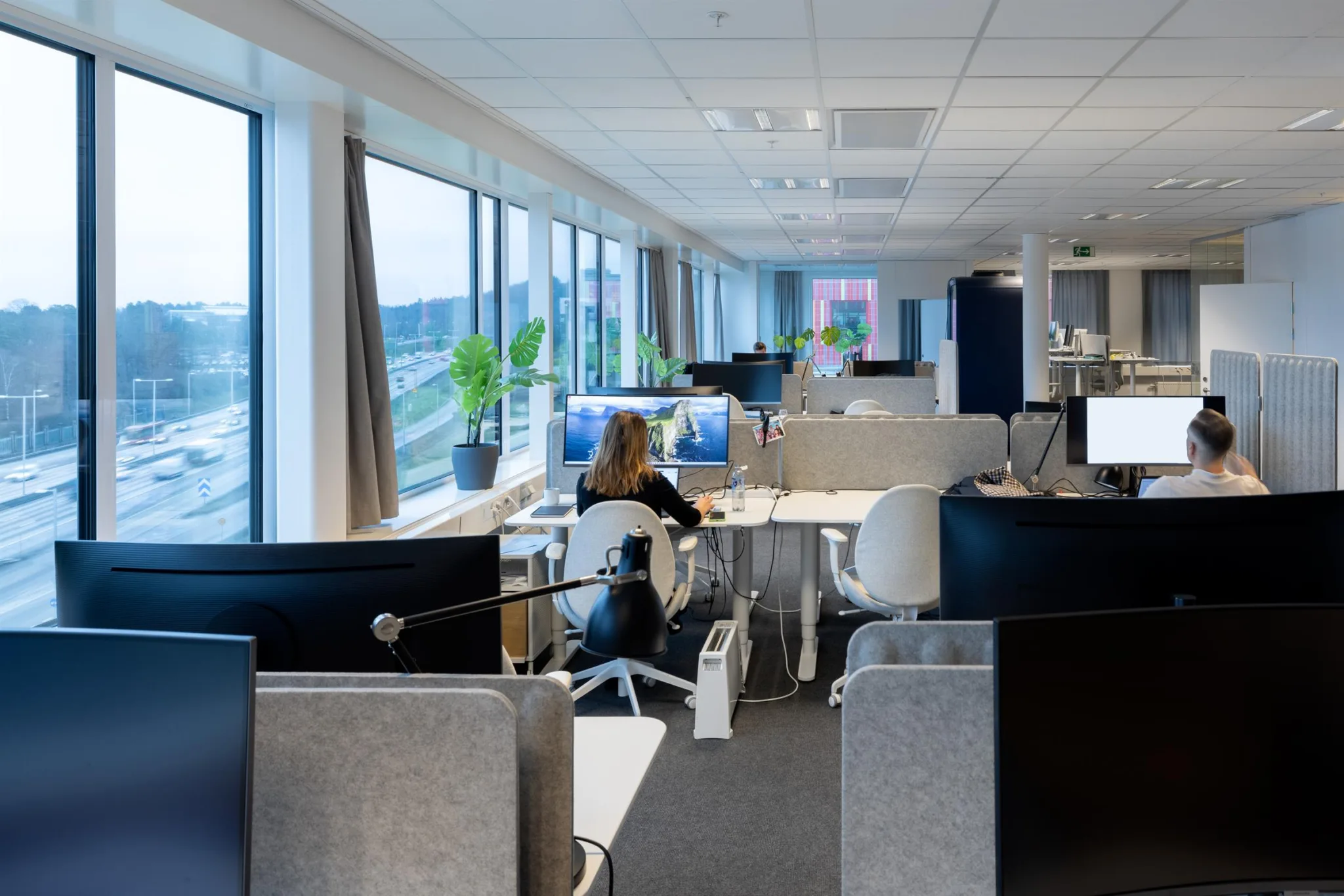 1. En ljus kontorsmiljö med flera arbetsstationer, stora fönster och utsikt mot en stadsmiljö.
