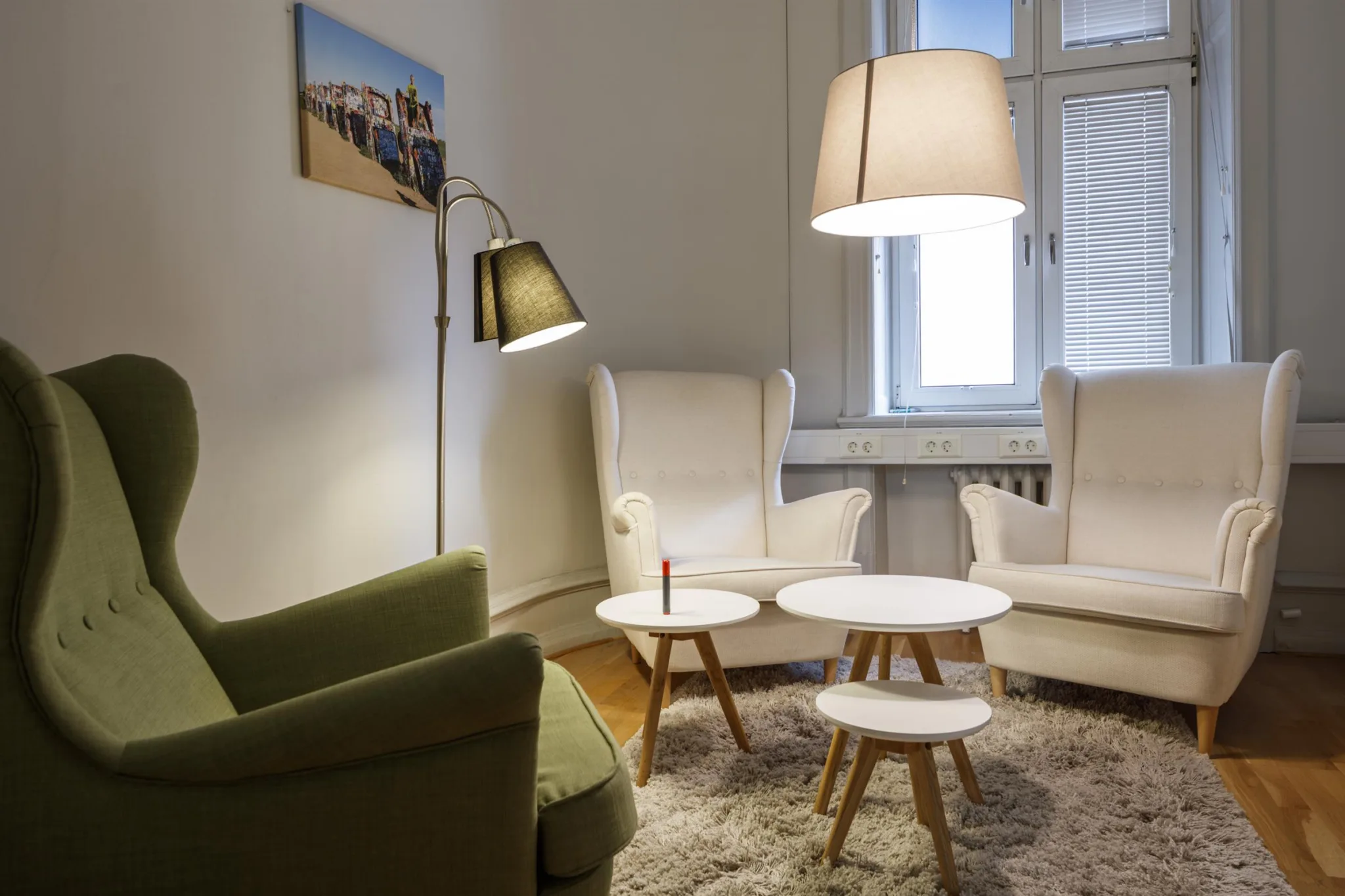 Ett vardagsrum med fåtöljer, ett soffbord, en matta, en golvlampa och väggdekorationer.