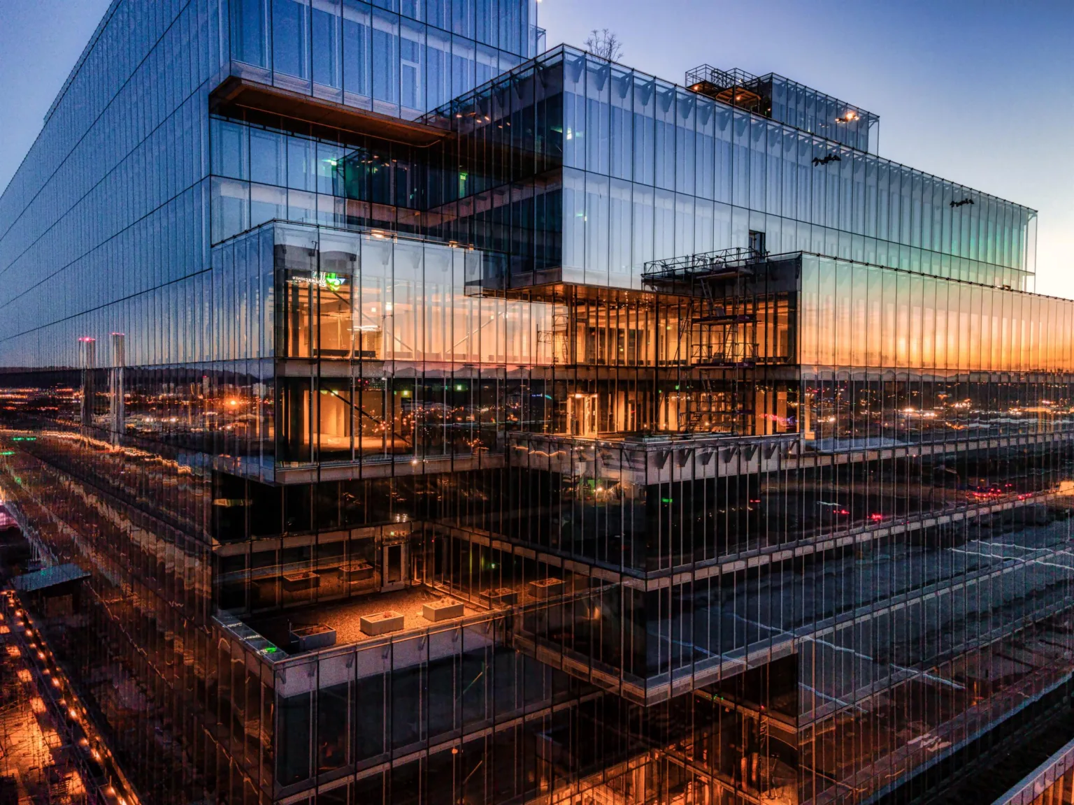 En byggnad med glasfasad, som reflekterar solnedgång och stadens ljus.