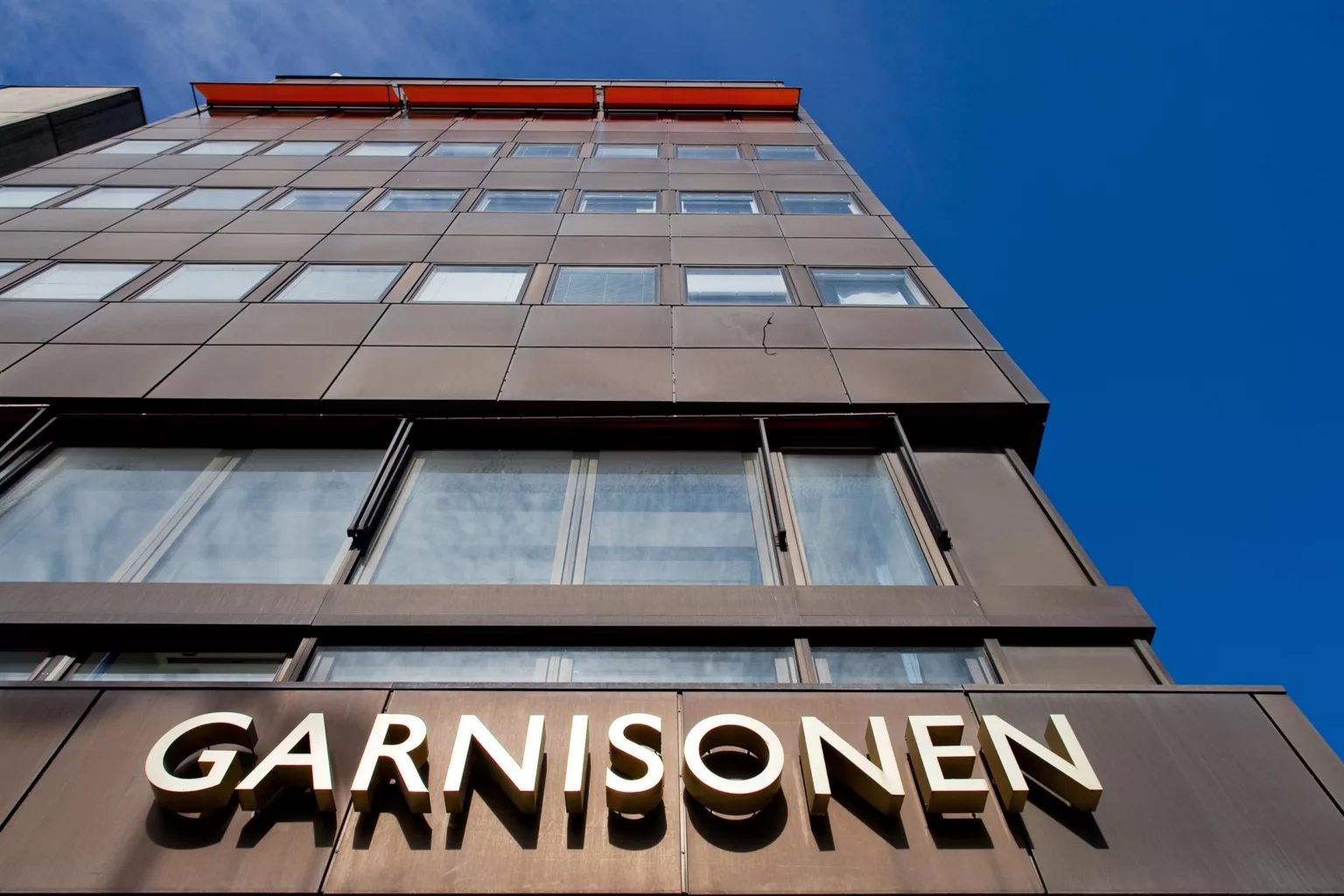 1. En modern byggnad med texten "Garnisonen" på fasaden mot en klarblå himmel.