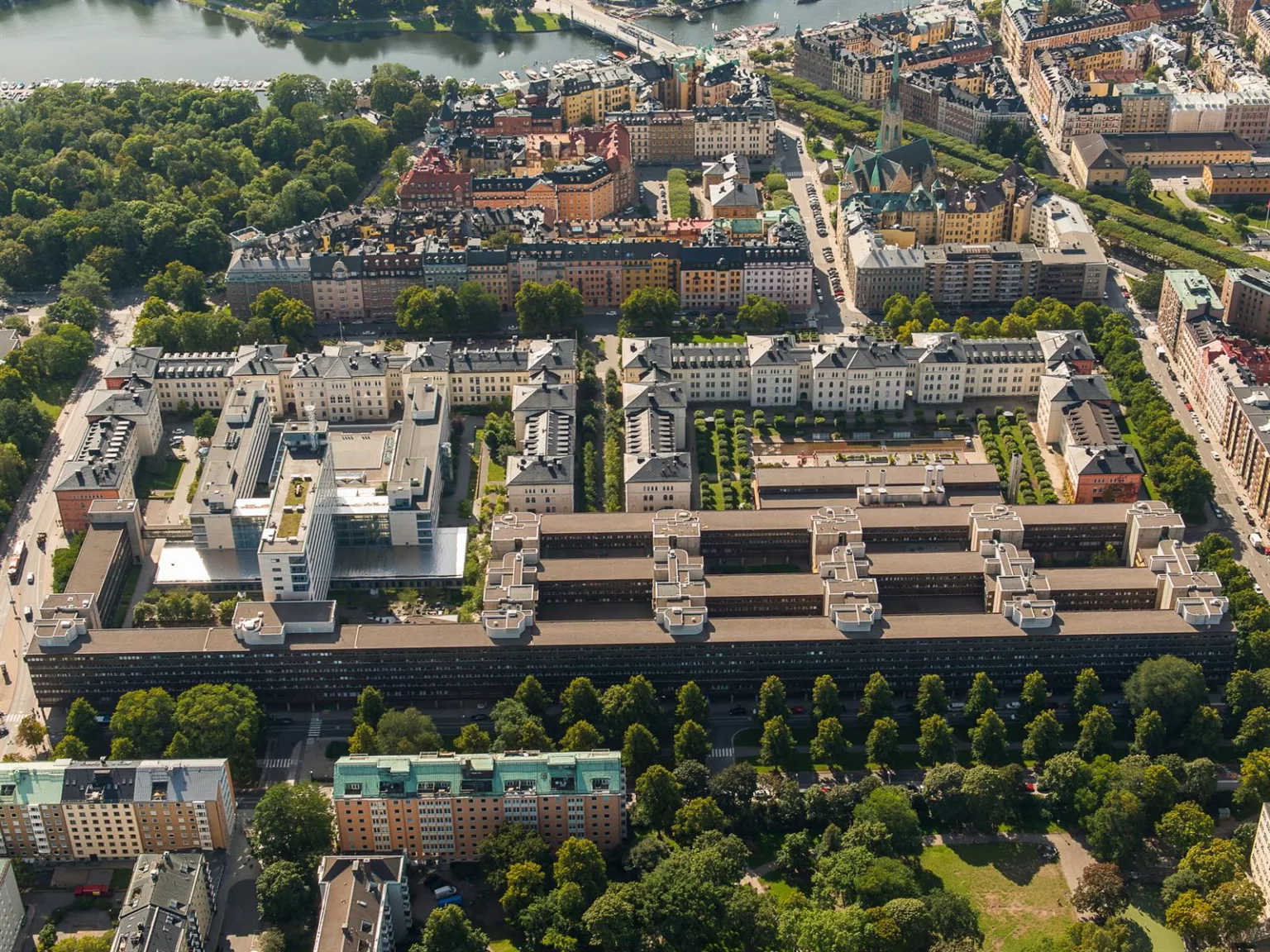 Flygfoto över en stadsdel med grönområden, byggnader och vägar i symmetrisk layout.