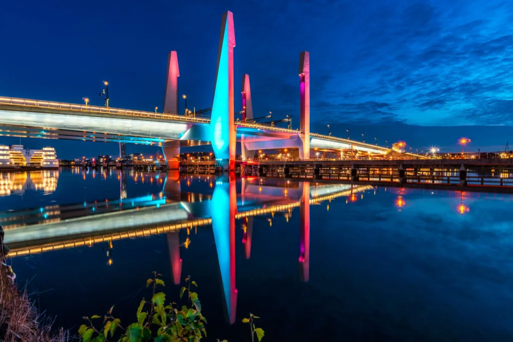 En bro med färgglada ljus som reflekteras i vattnet under en klar natt.