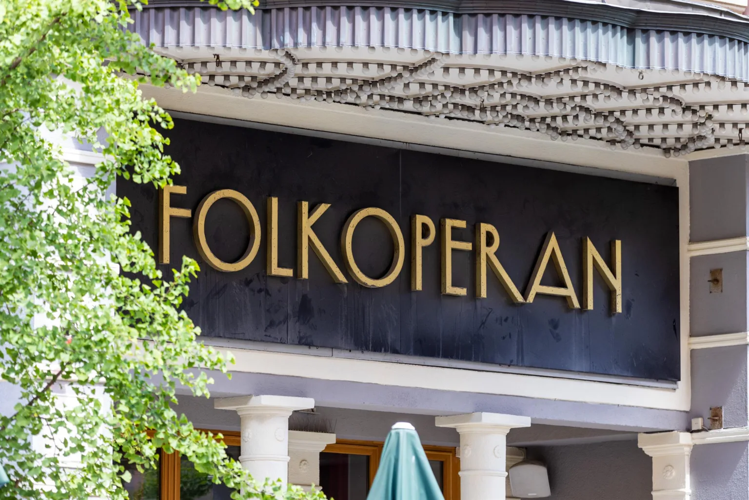 4. En byggnad med en svart skylt och texten "Folkoperan" i guld, omgiven av grönska.