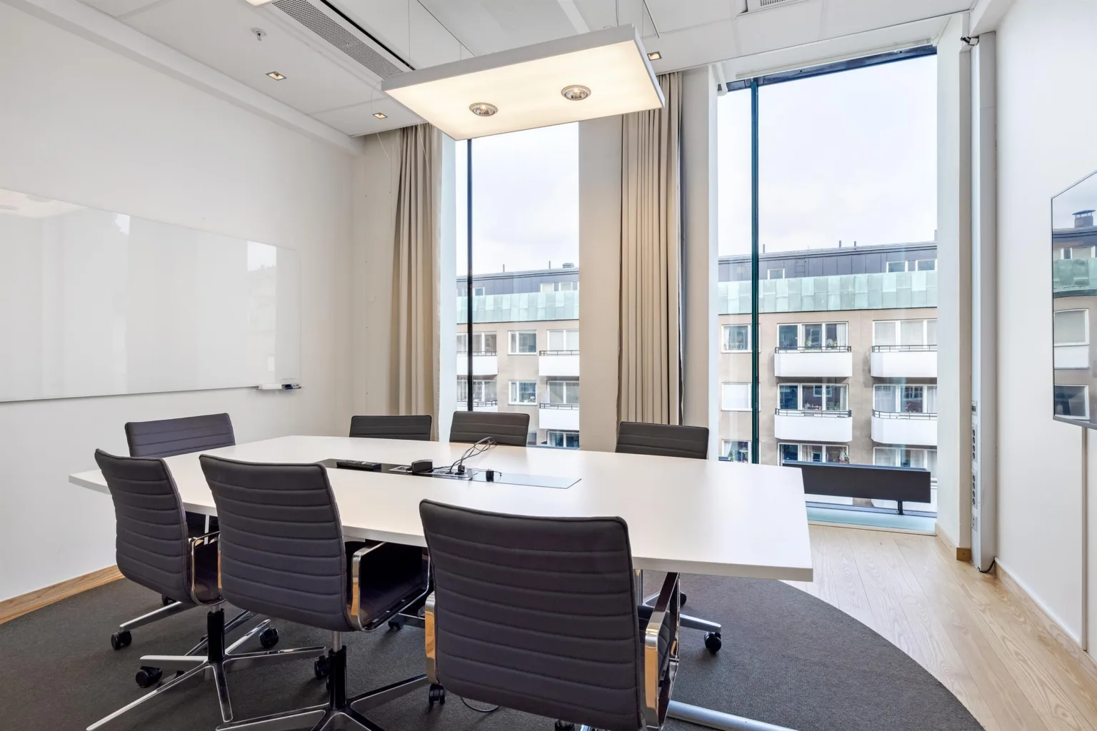 2. Ett konferensrum med ett stort bord, sex stolar och stora fönster med utsikt över byggnader.
