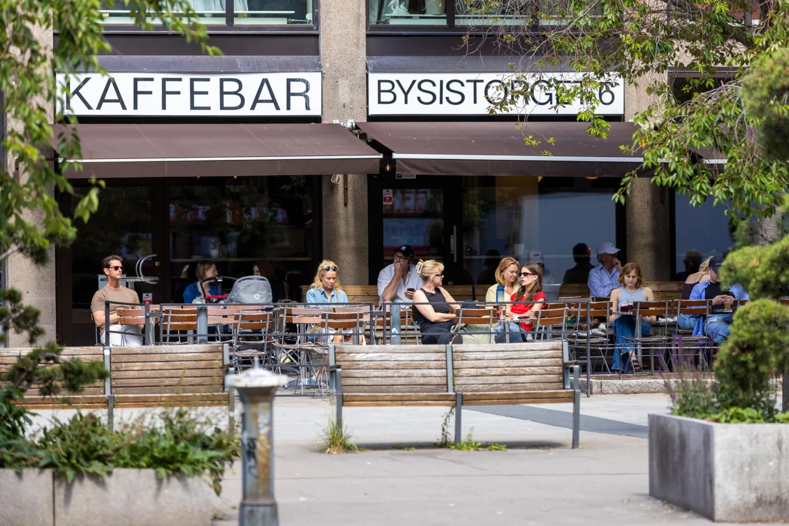 1. Utomhusservering vid ett kafé med skyltar som visar "Kaffebar" och "Bysistorgets", där människor sitter på uteserveringen.