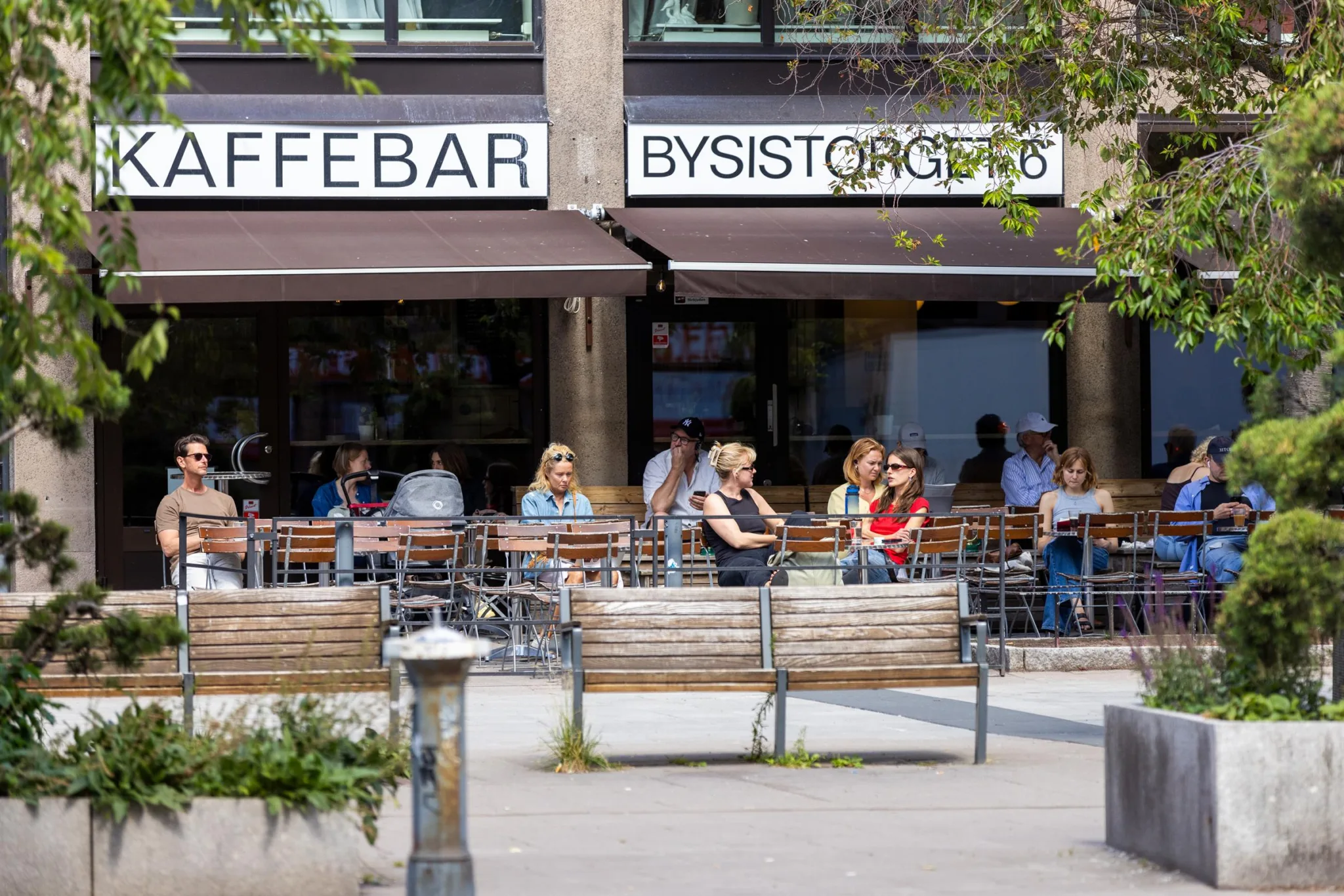 1. Utomhusservering vid ett kafé med skyltar som visar "Kaffebar" och "Bysistorgets", där människor sitter på uteserveringen.