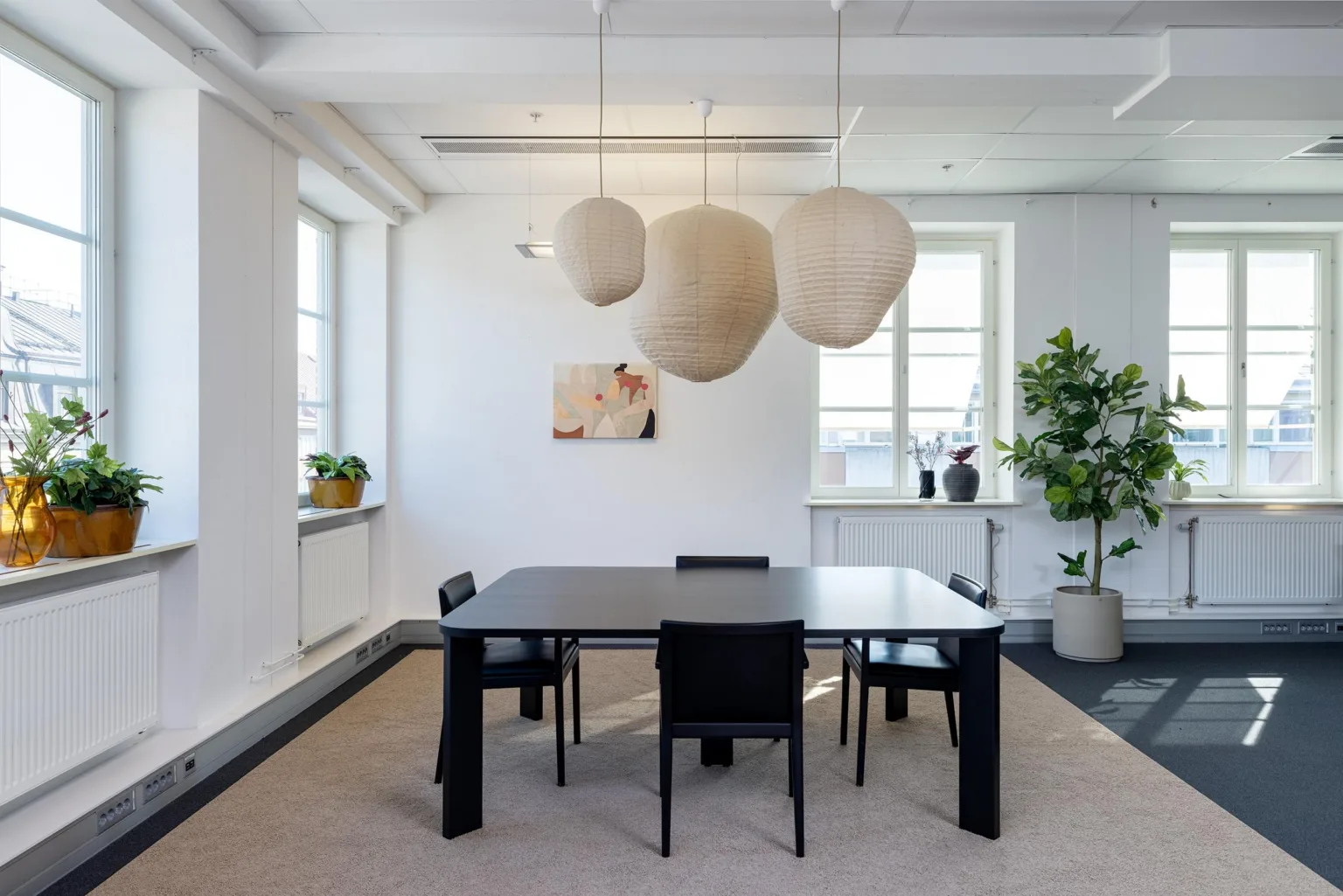 3. Minimalistiskt mötesrum med ett svart bord, fyra stolar och stora, vita hänglampor ovanför.