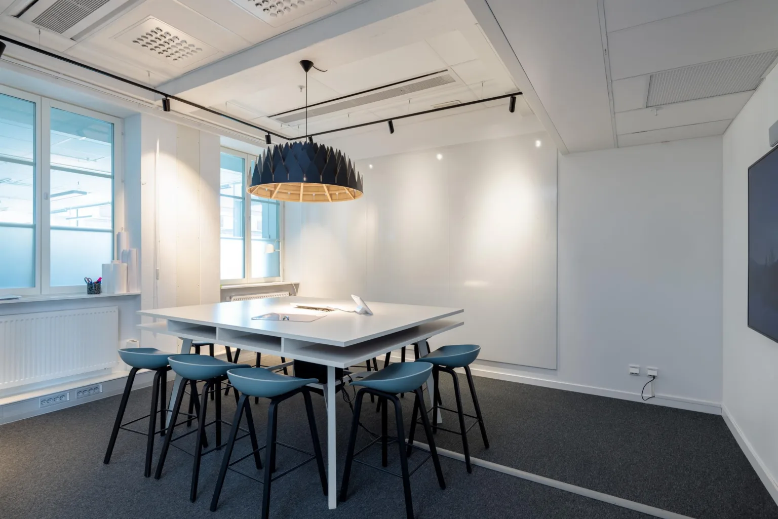 4. Ett modernt mötesrum med ett stort vitt bord omgivet av blå stolar och en hängande lampa ovanför.